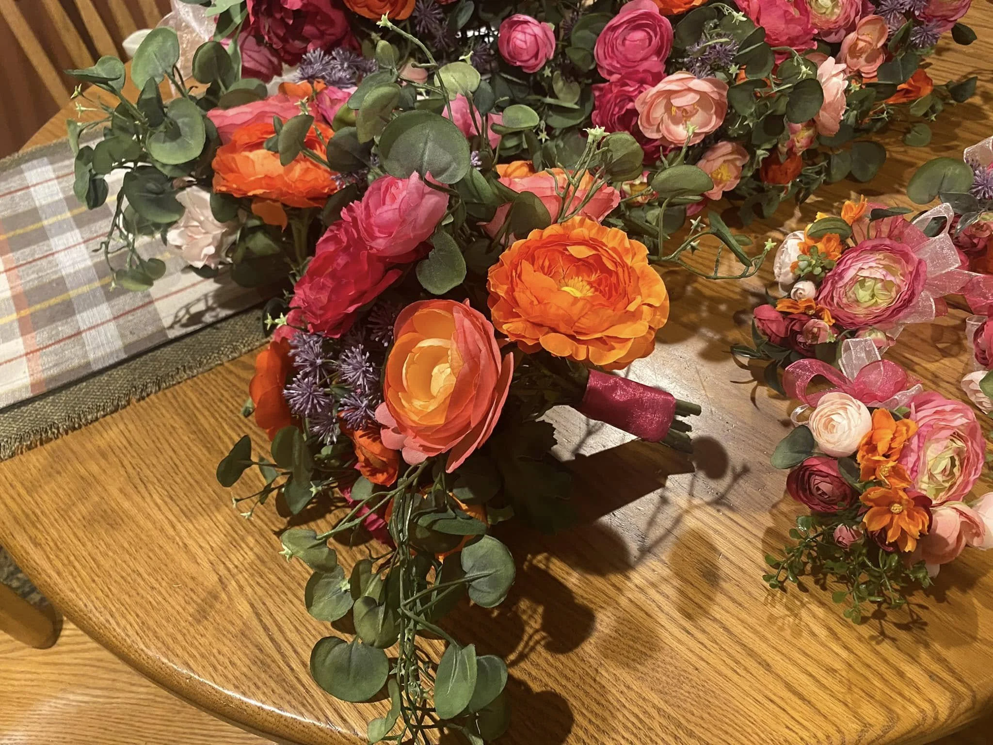 A colorful bouquet of artificial flowers including orange, pink, and purple blooms, with green foliage, on a wooden table.