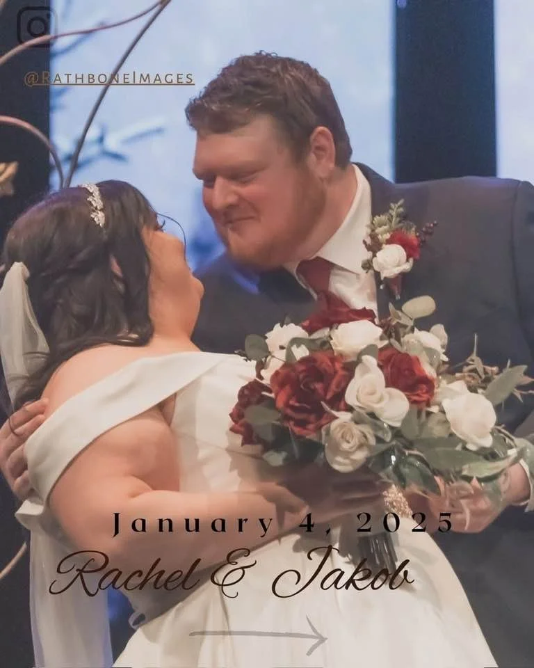 A bride and groom are sharing a moment during their wedding, with the groom holding a bouquet of red and white flowers. The bride's name is Rachel and the groom's name is Jakub, and the wedding date is January 4, 2025.