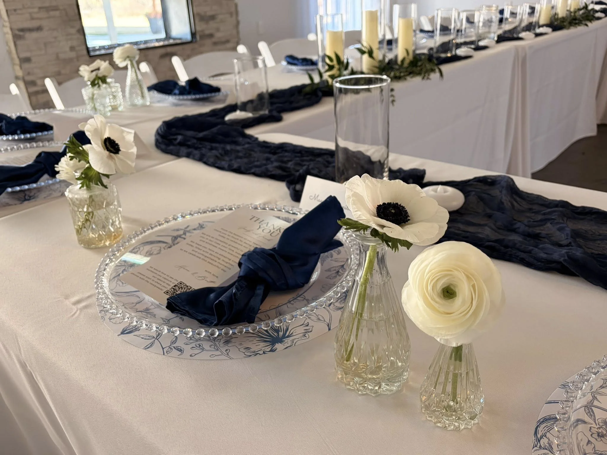Elegant table setting with navy blue napkins, white flowers in glass vases, and a navy table runner at a formal event.