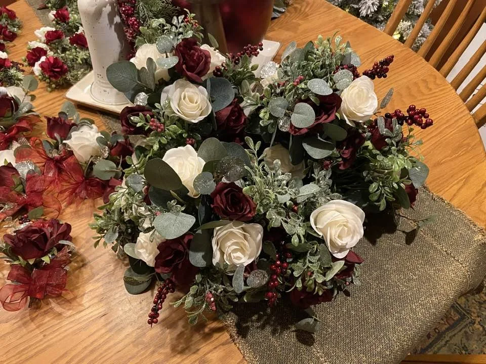 A floral arrangement with white and dark red roses, green leaves, and red berries on a wooden table.