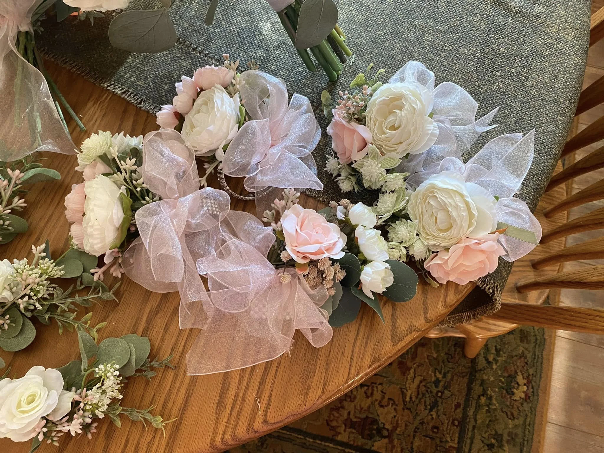 Corsages with white and blush pink flowers, green leaves, and pink translucent bows on a wooden table