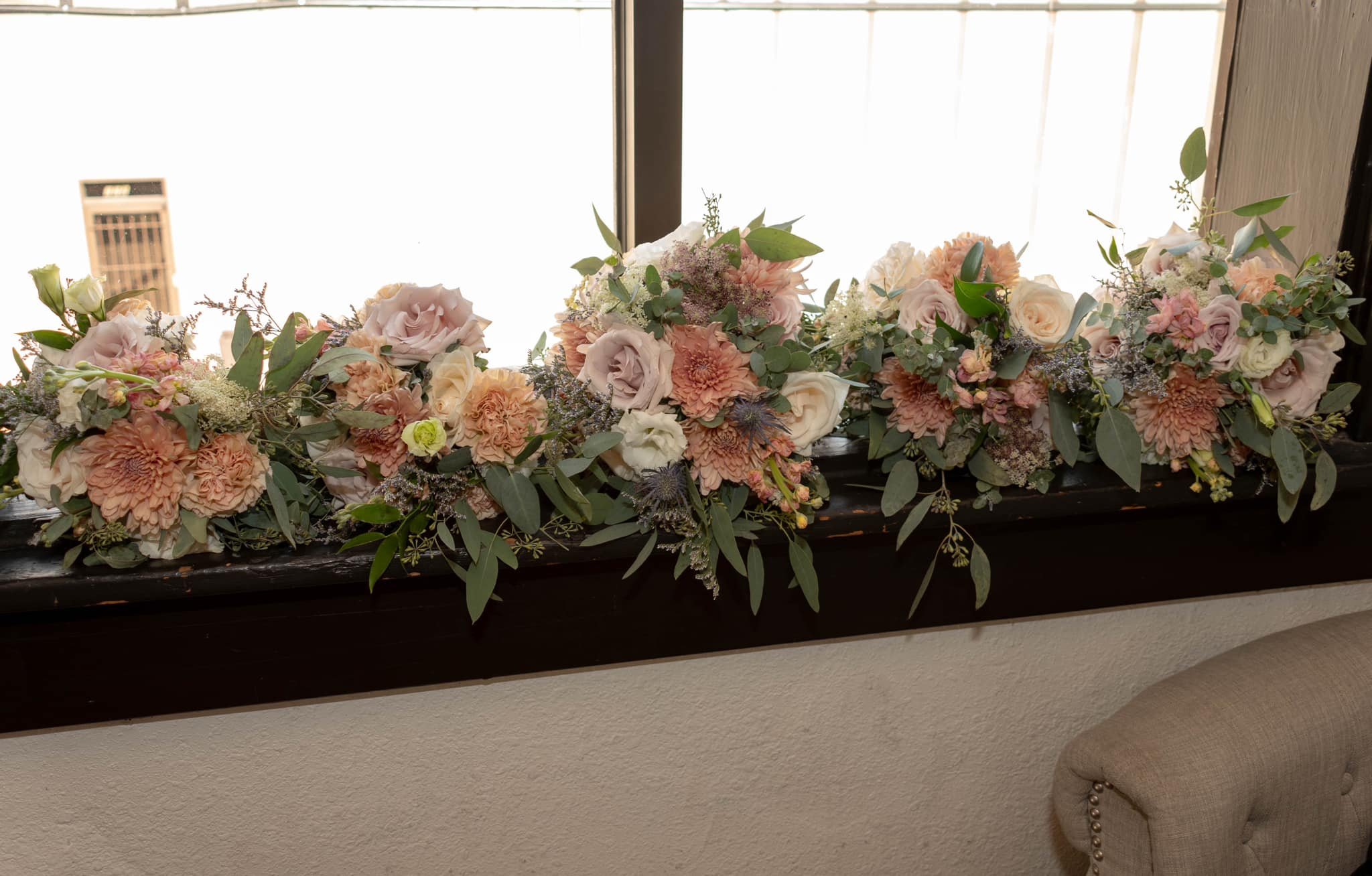 A floral arrangement of peach, pink, and white flowers with greenery on a black window ledge.