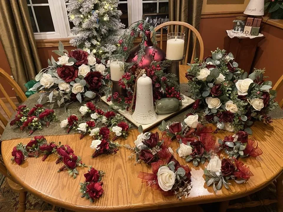 A decorated Christmas table with flower arrangements, candles, a large red and pink Christmas ornament, and a Christmas tree in the background.