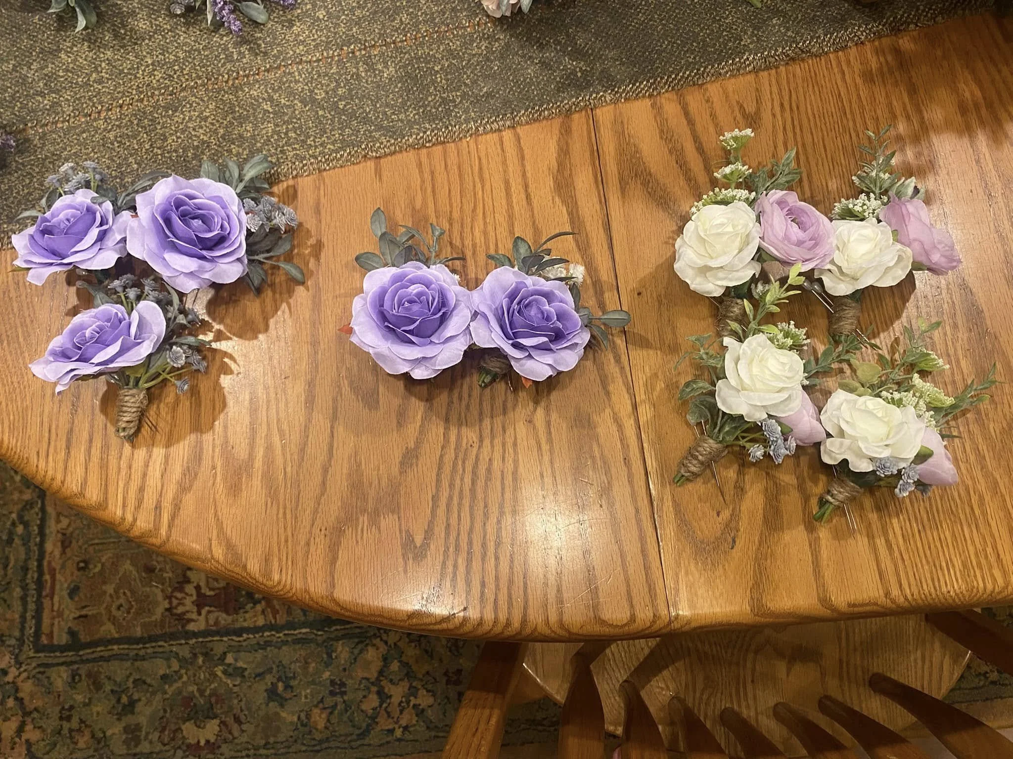Three sets of floral boutonnieres with purple, white, and pink flowers placed on a wooden table.