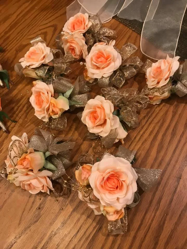 Corsages made of peach roses, gold glittery ribbons, and small decorative beads.