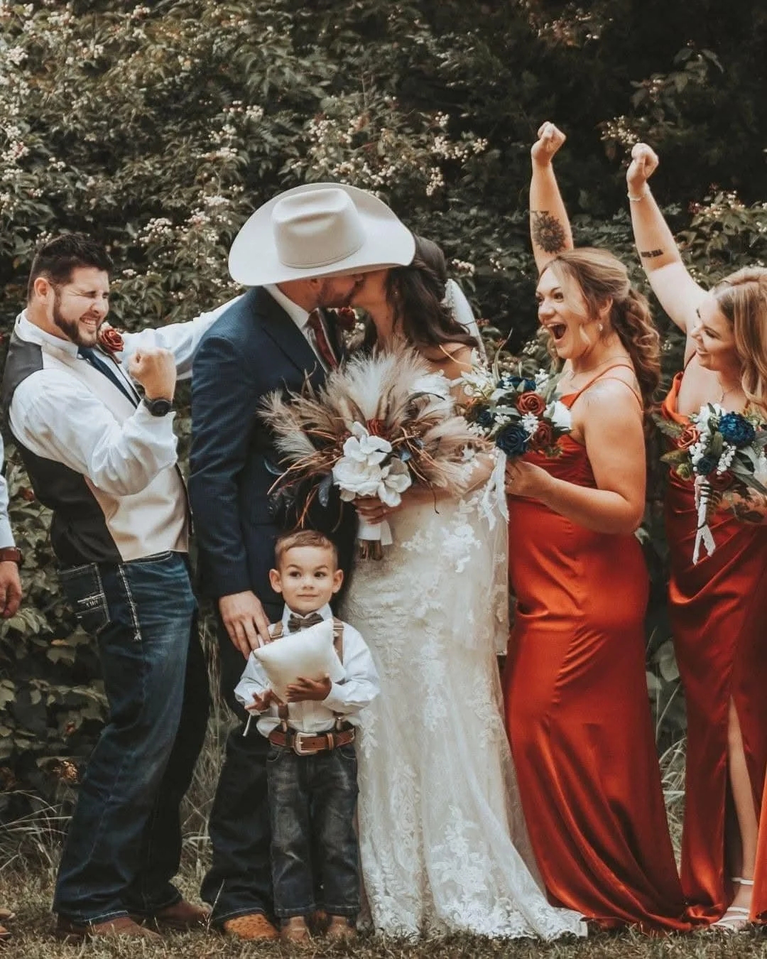 A wedding celebration with a bride and groom sharing a kiss, surrounded by joyful bridesmaids and groomsmen outdoors.