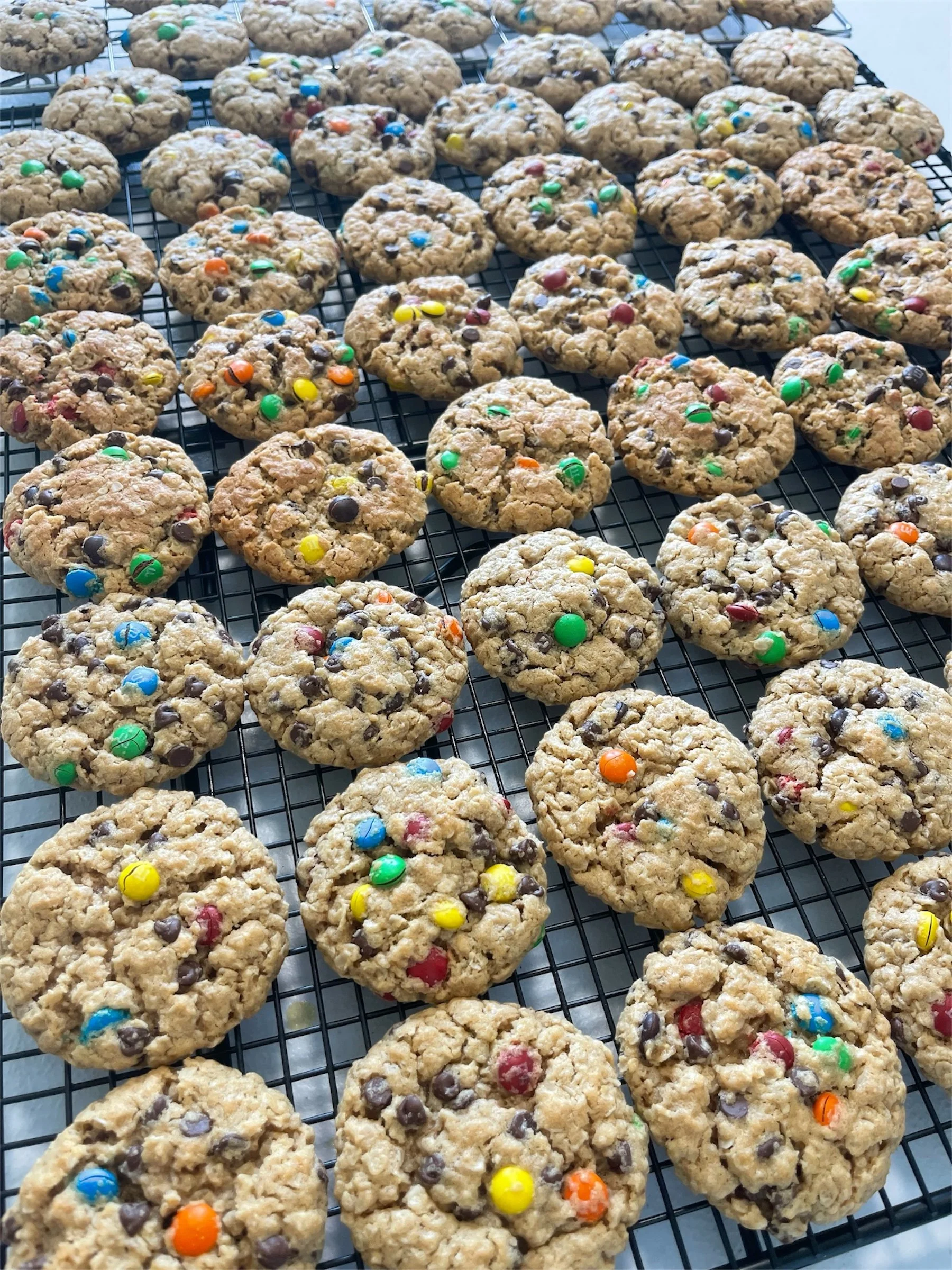 A cooling rack filled with freshly baked oatmeal cookies with colorful candy-coated chocolate pieces.