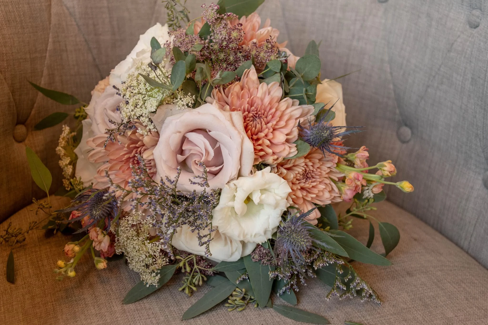 A bouquet of pink, white, and purple flowers with green leaves on a tufted gray and brown fabric surface.