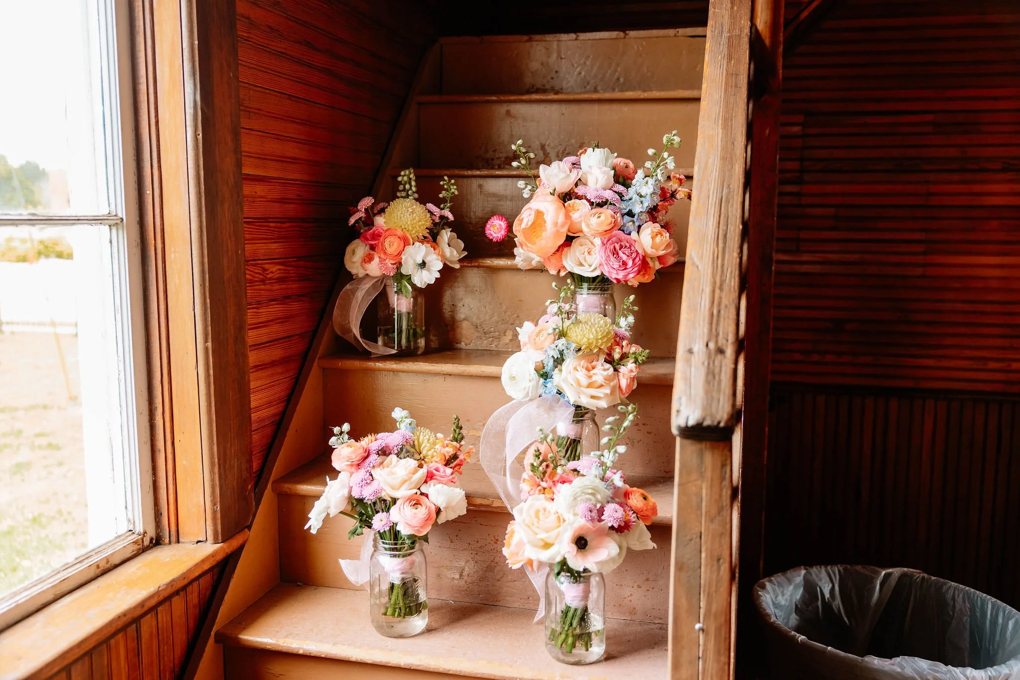 Vase filled with pink, peach, and white flowers on a wooden staircase