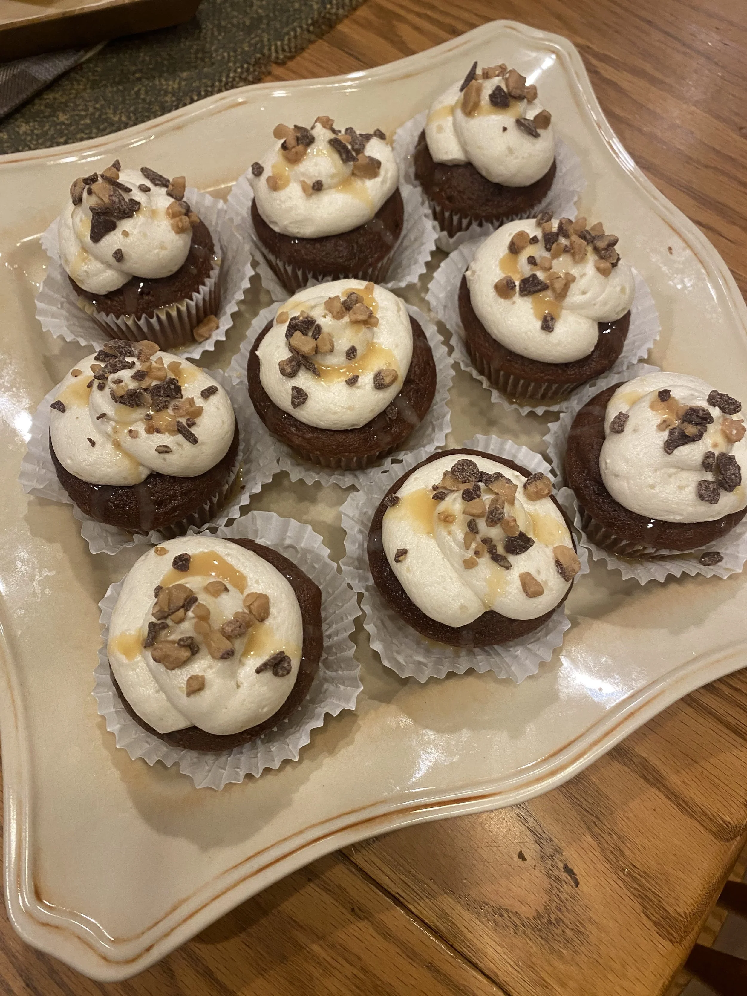 Chocolate cupcakes topped with white frosting and sprinkled with chopped nuts, arranged on an off-white platter.