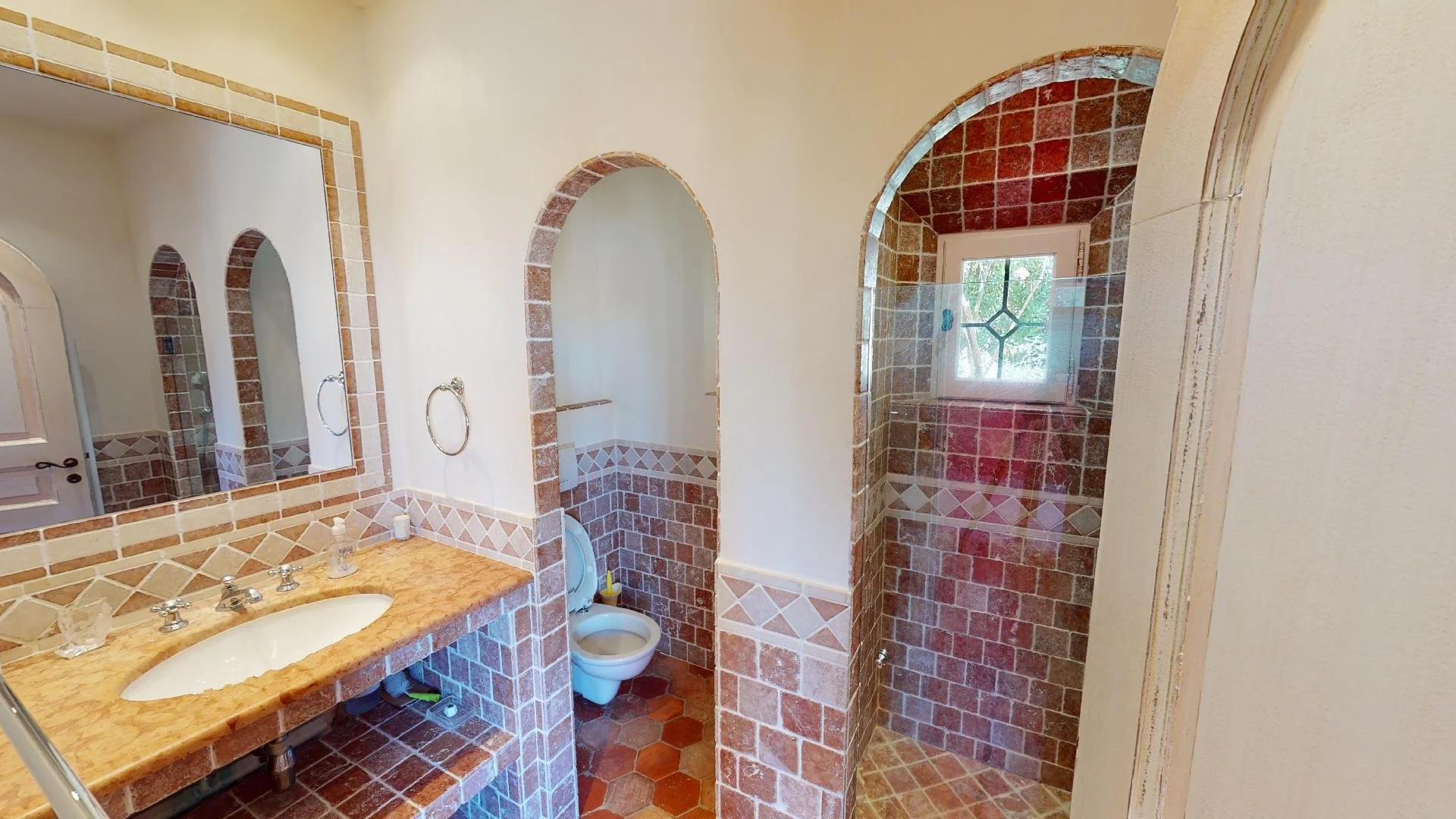 A bathroom with a tiled vanity, mirror, toilet, and walks-in shower with a window.