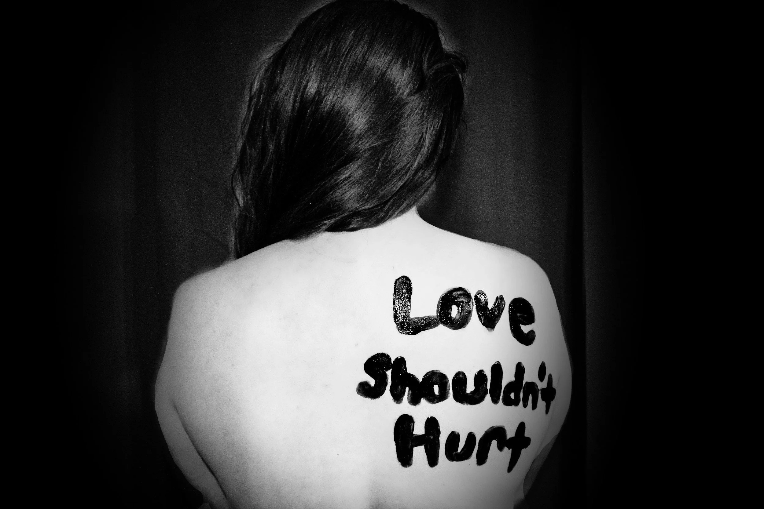 Back of a person with dark hair, shoulder exposed, with the words 'Love' and 'Yourself' written on their back in black lettering.