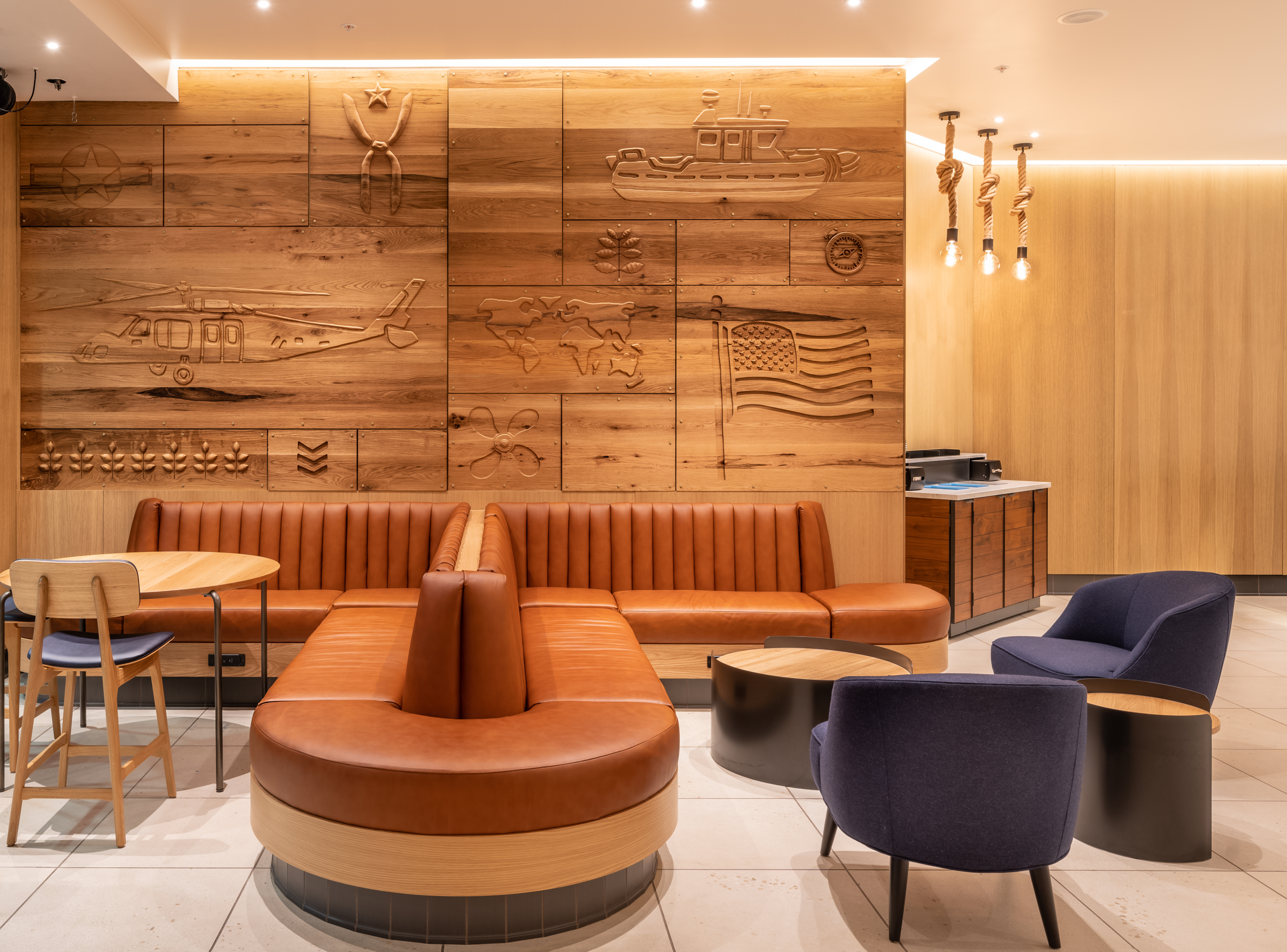 Modern lounge area with wood-paneled walls, leather and fabric chairs, and decorative wall art featuring military and patriotic themes, including an American flag and helicopters.
