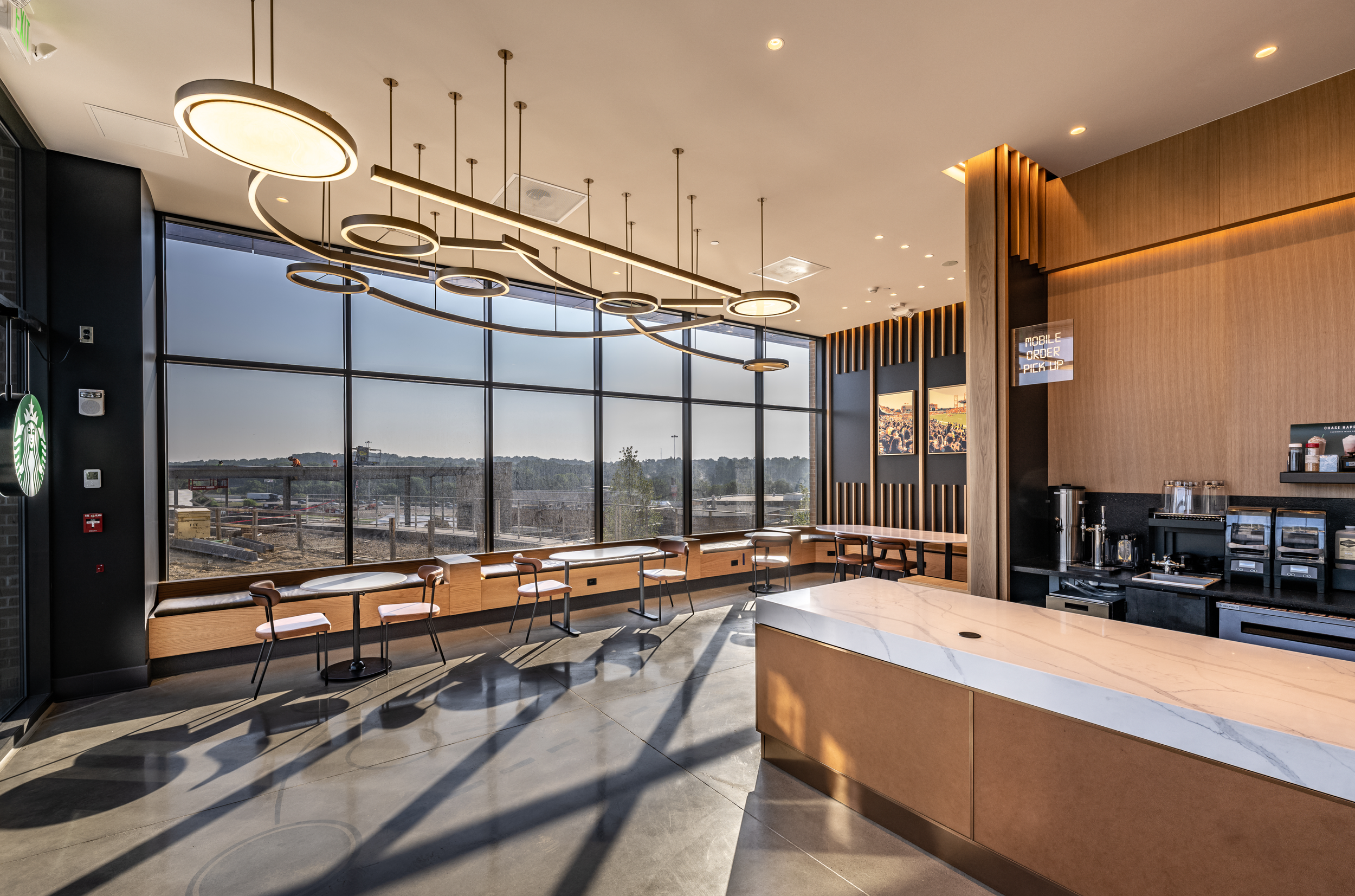 Interior of a modern coffee shop with large windows, minimalist furniture, and stylish lighting fixtures.
