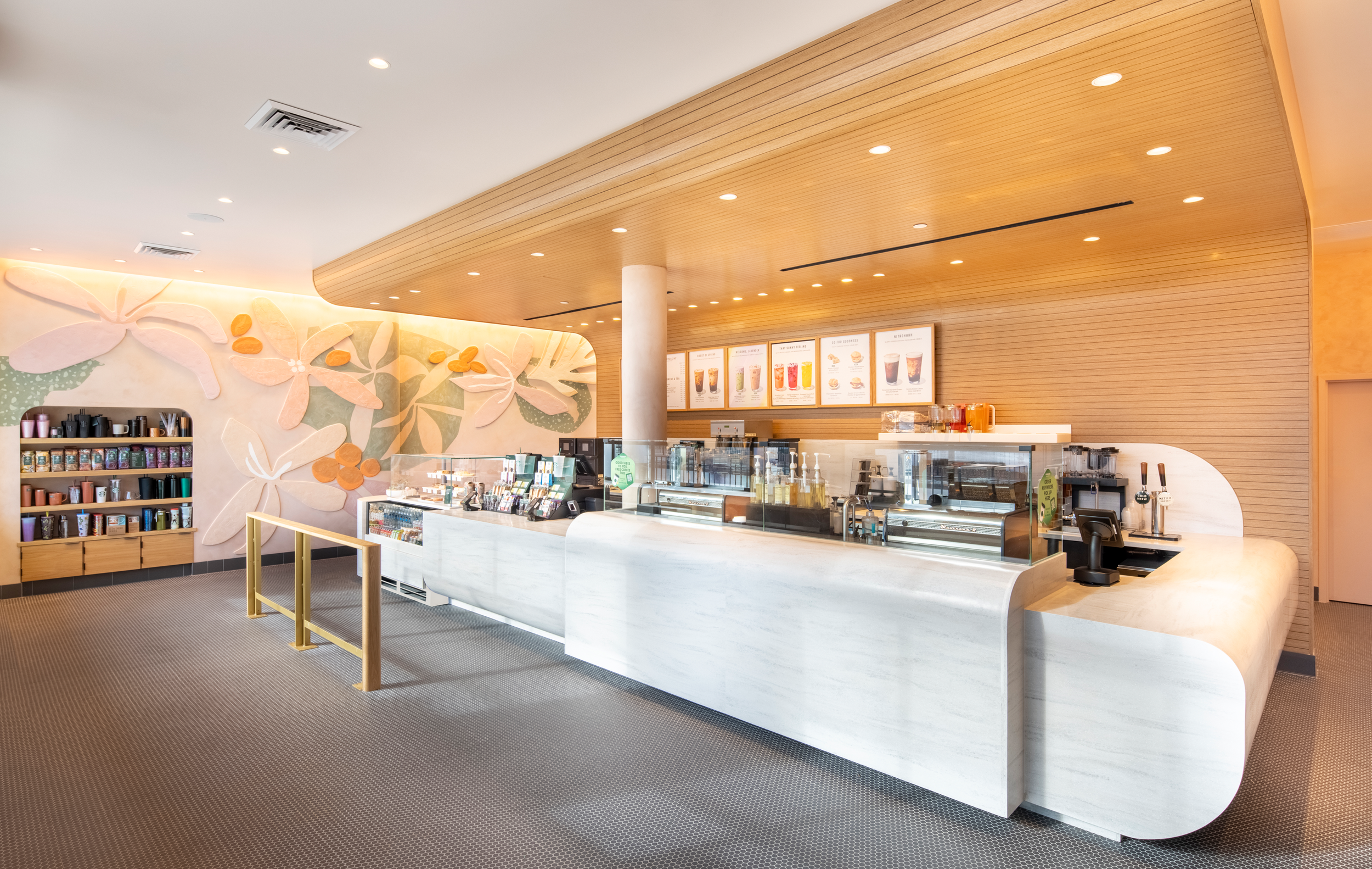 Empty coffee shop counter with drink menu boards, coffee machines, and colorful wall art of abstract flowers and leaves.