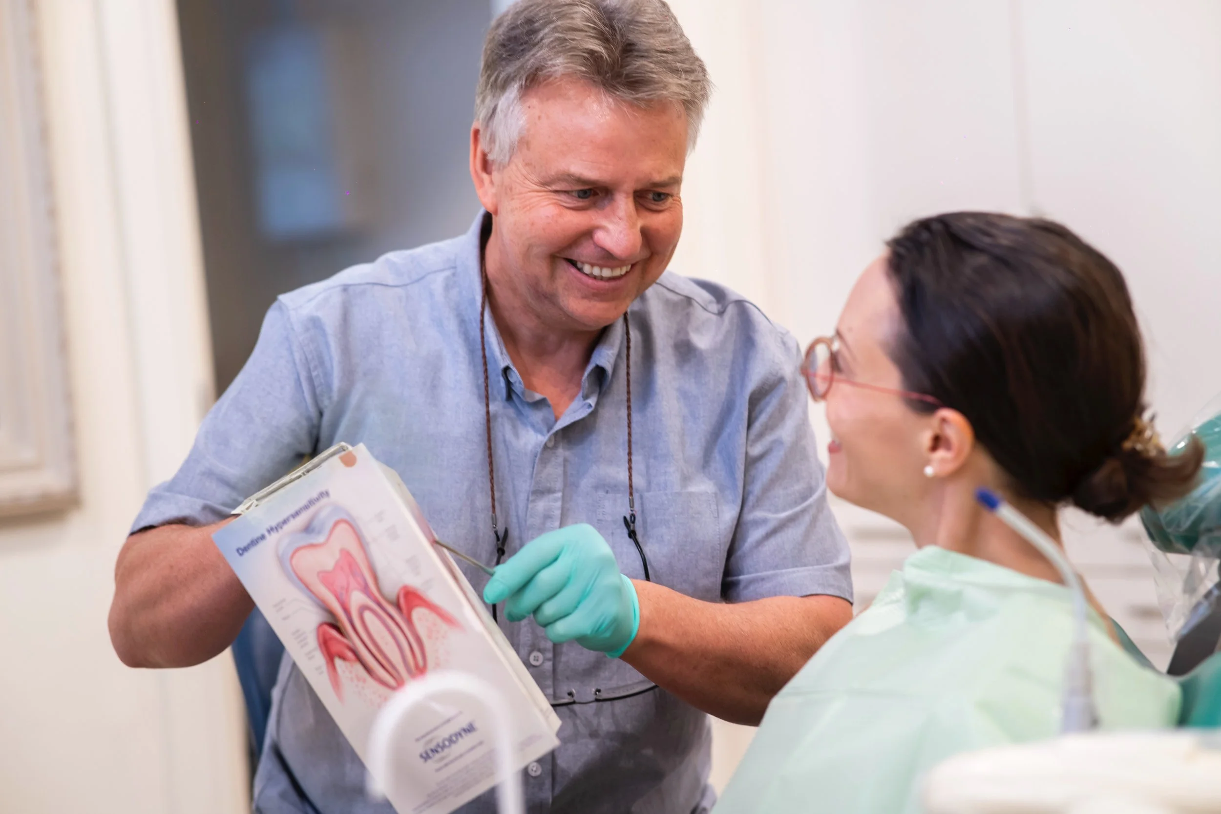 A male dentist showing a diagram of teeth to a female patient in a dental office.