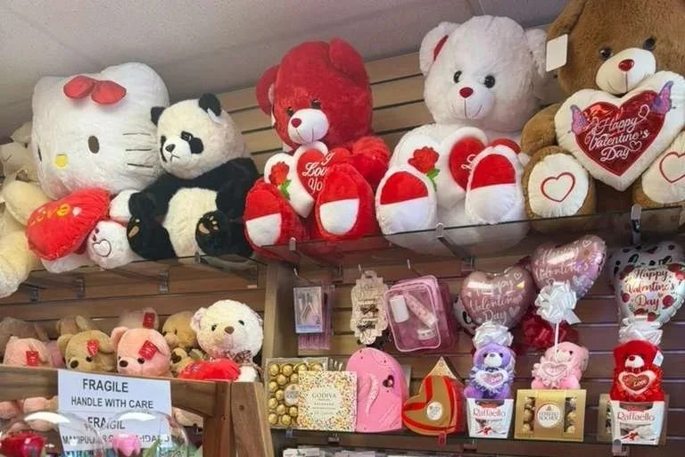 A collection of Valentine's Day plush teddy bears and heart-shaped gifts displayed on shelves and a table, including Hello Kitty and panda bears.