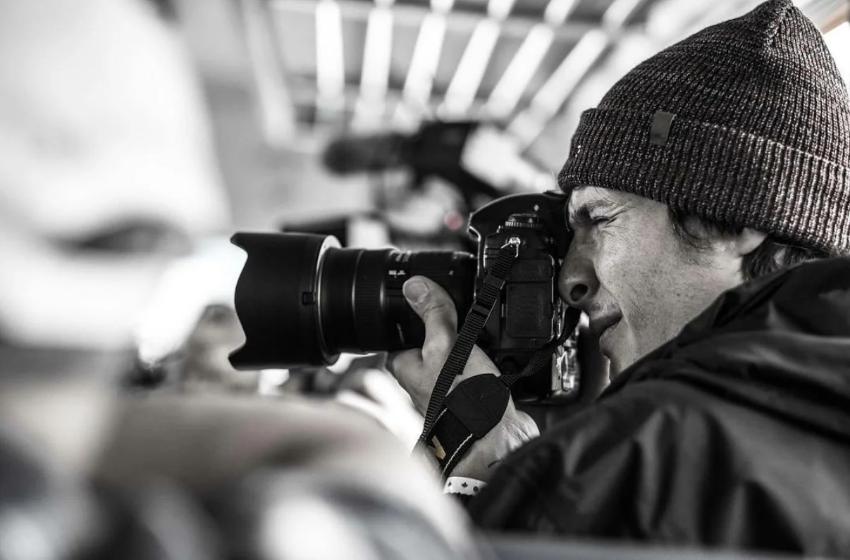 A man wearing a beanie hat is taking a photograph with a camera.
