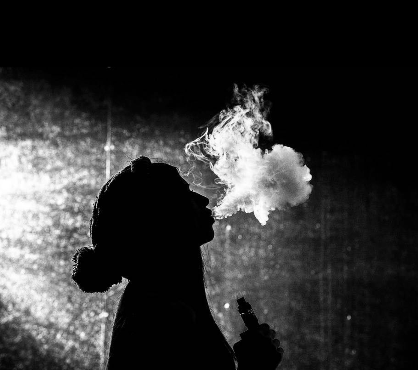 Silhouette of a person with a bun hairstyle exhaling vapor or smoke, holding a vape or electronic cigarette, against a dark, textured background.