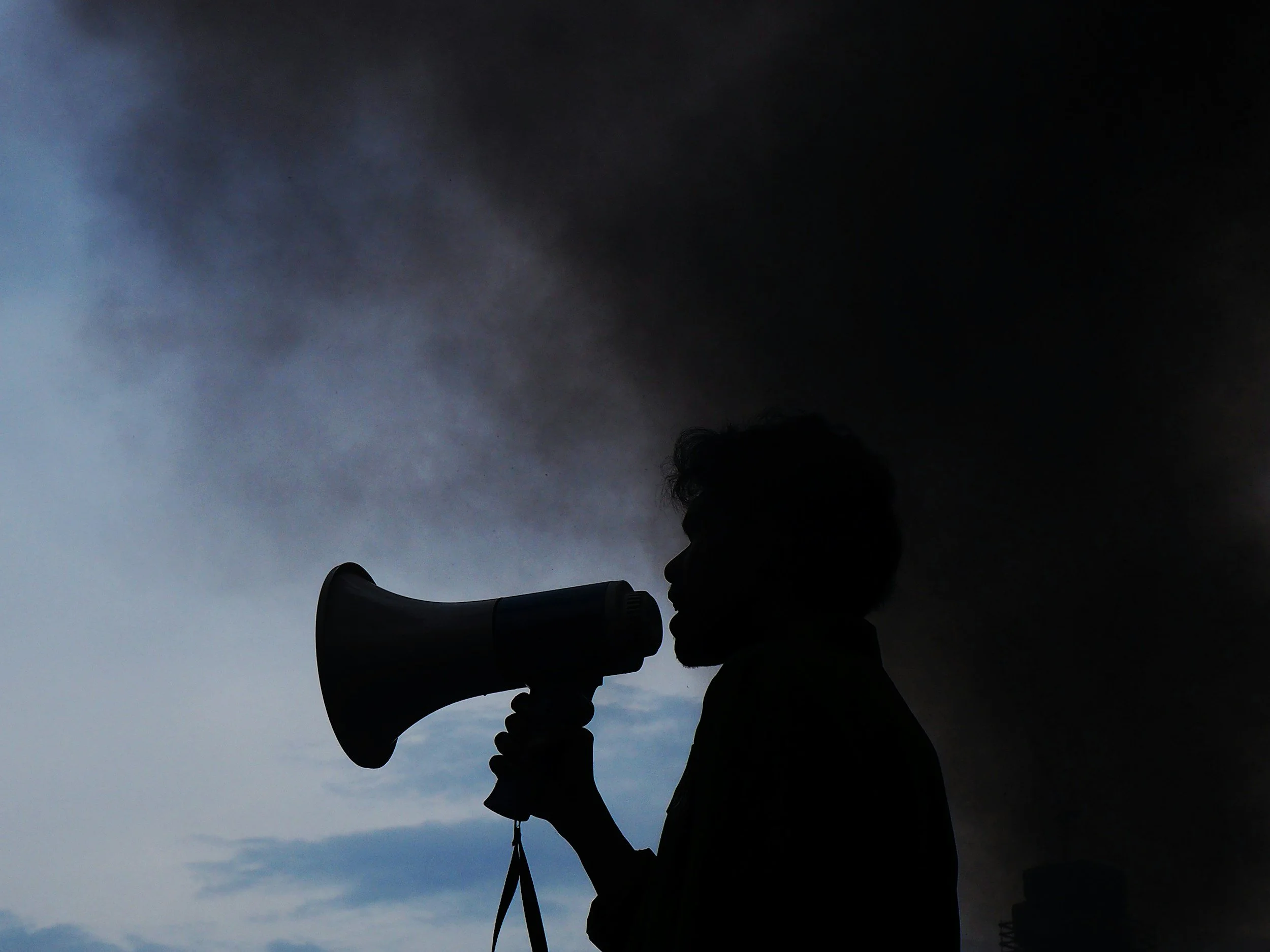 Silhouette of a person holding a megaphone against a cloudy sky.