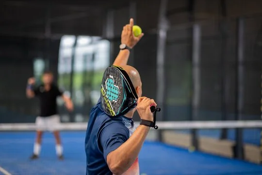 Un joueur de tennis de table en action, prêt à servir avec sa raquette et une balle, dans une salle intérieure.