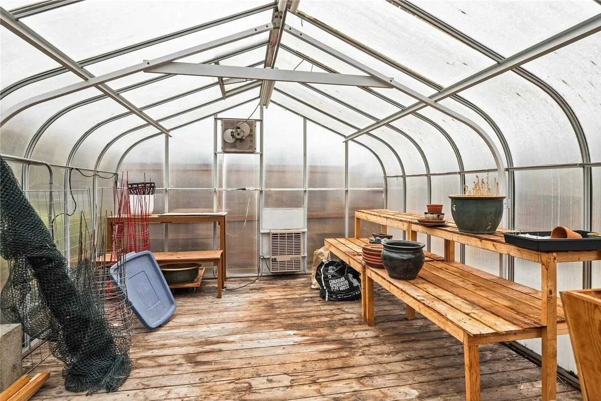 Empty greenhouse with wooden benches, pots, gardening tools, and an air conditioning unit