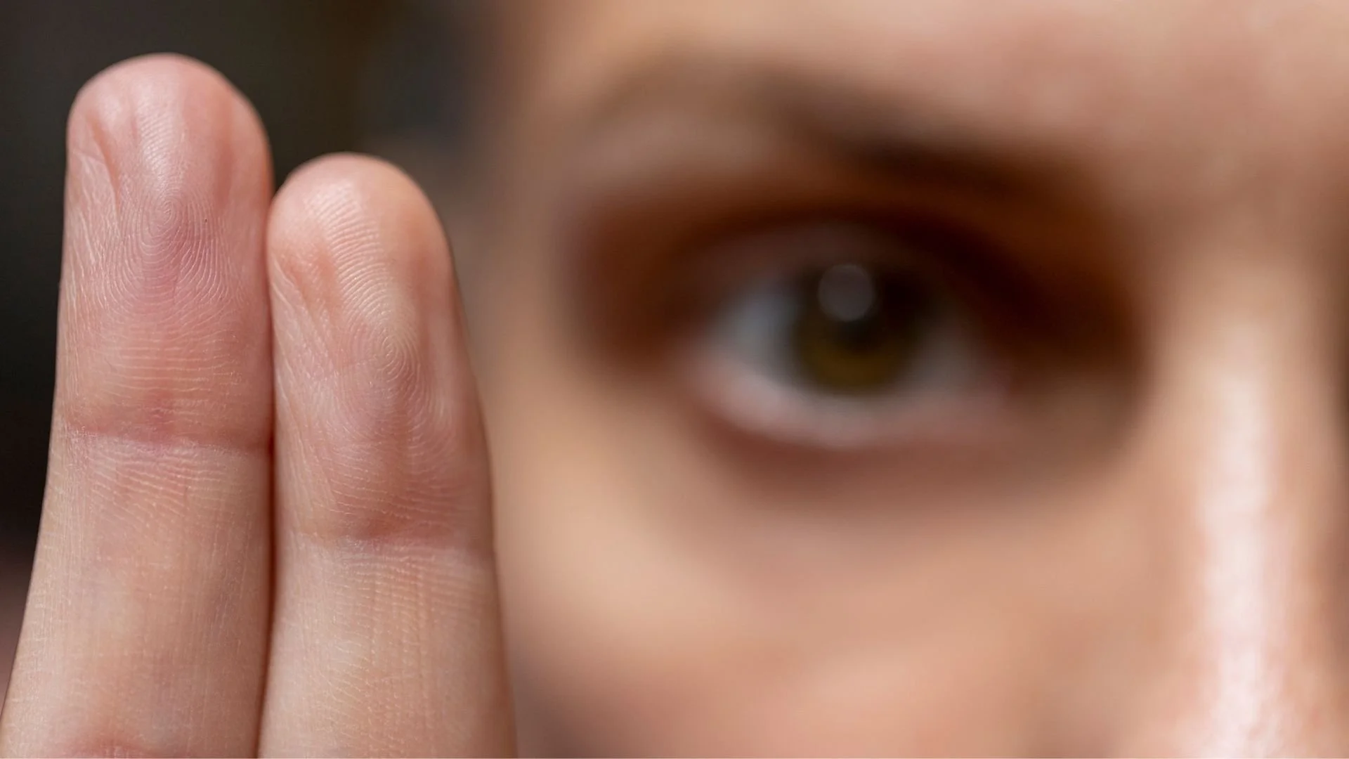 Close-up of a person's face with focus on their eye and fingers held up near the face.