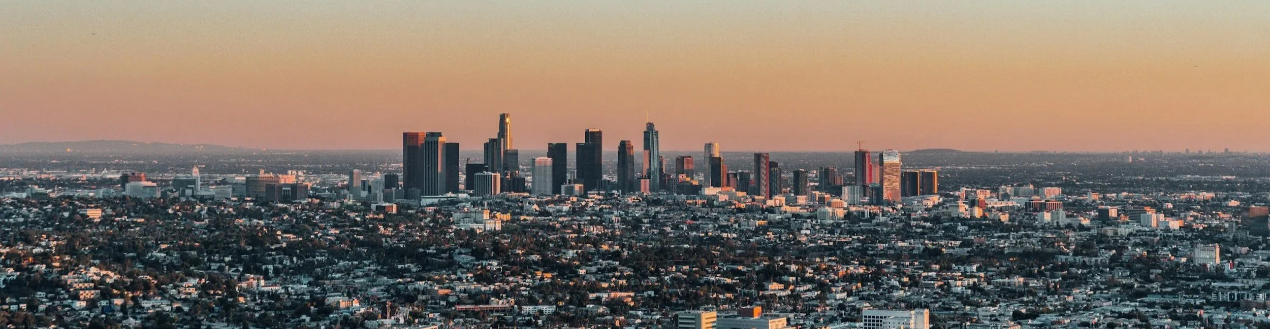 Aerial view of downtown Los Angeles at sunset with tall skyscrapers and city buildings.