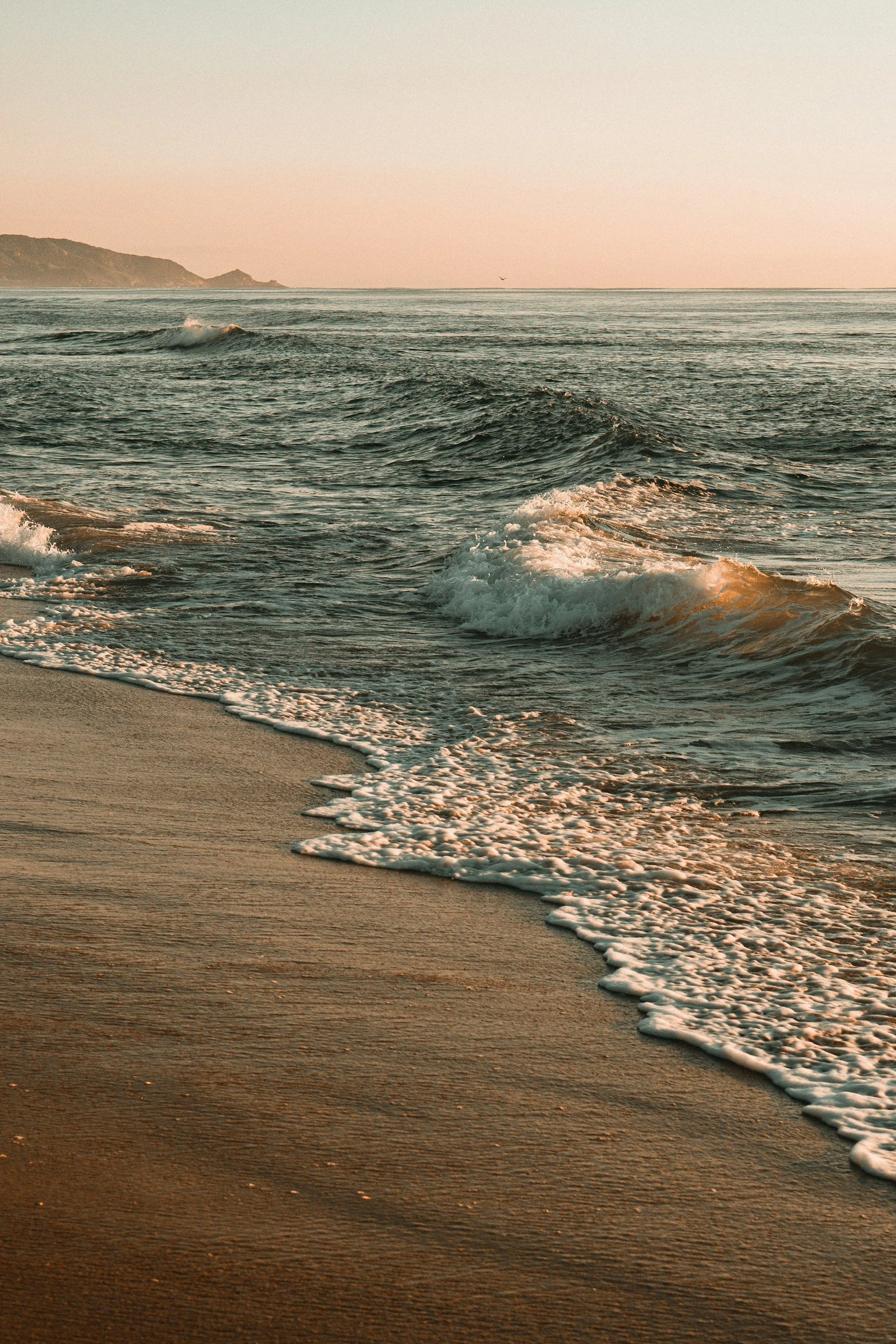 Sunset at the beach with gentle waves hitting the sandy shoreline.