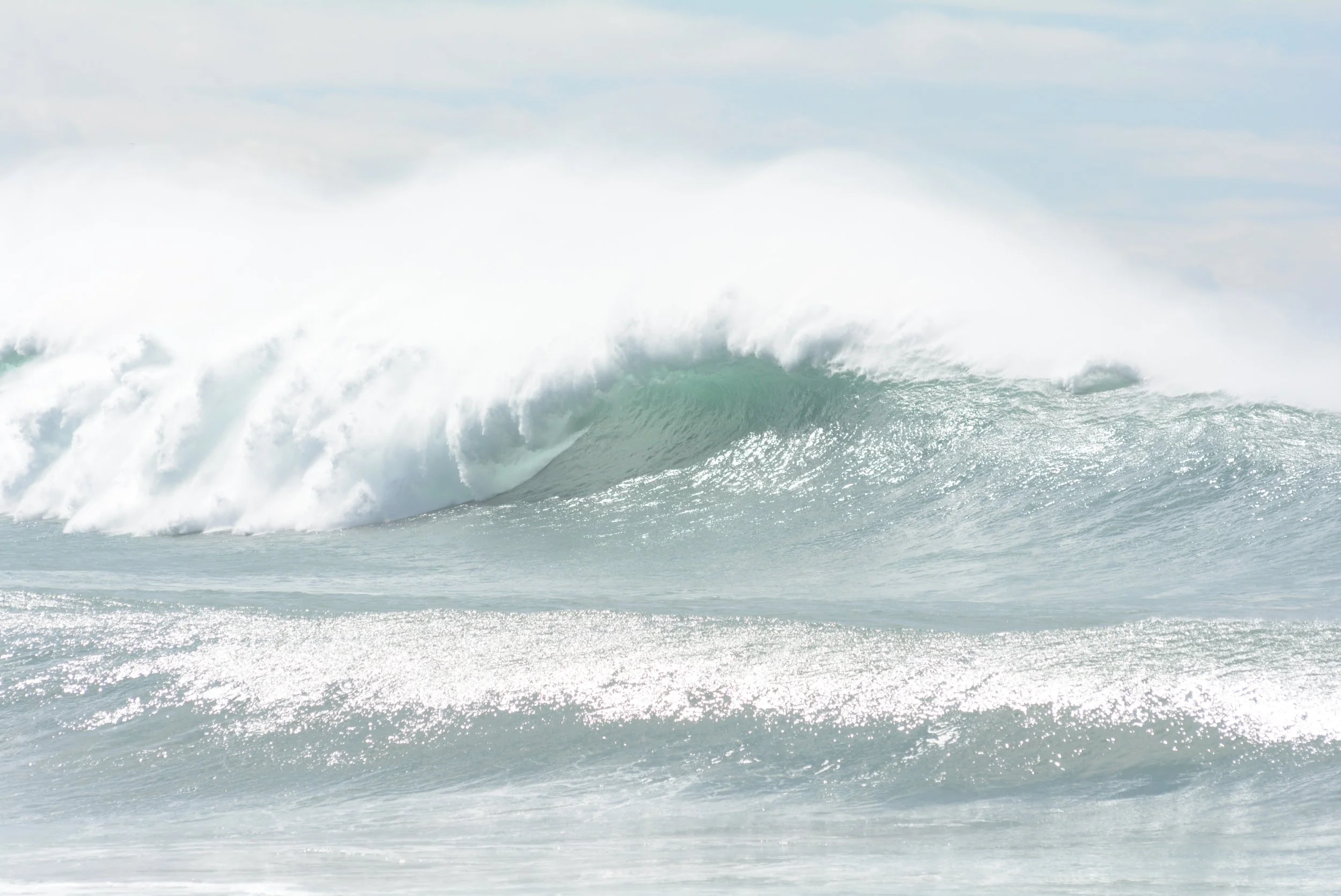 Large ocean wave with white and green colors crashing in the sea against a cloudy sky