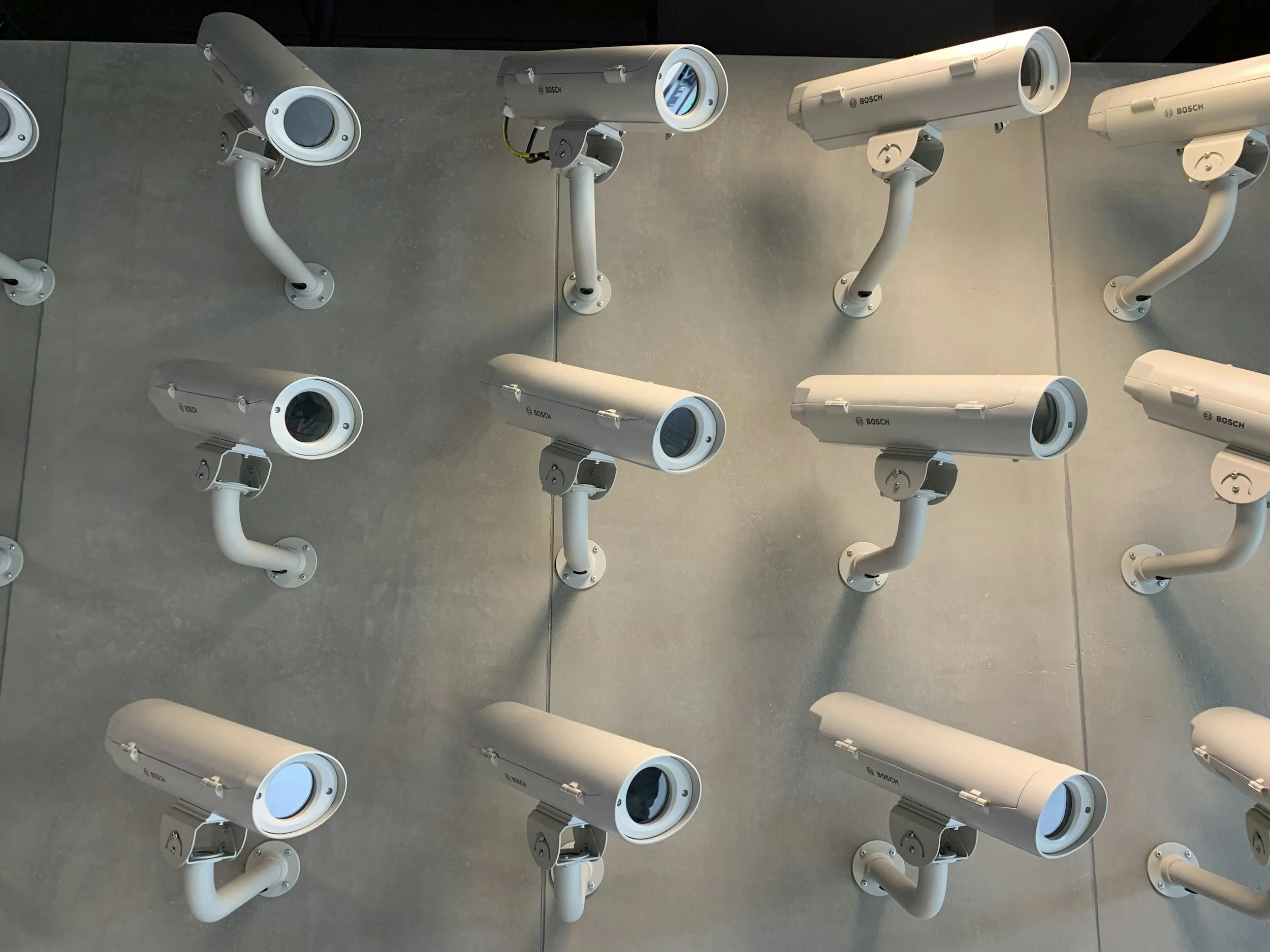 Multiple white security cameras mounted on a ceiling, facing downward, with some cameras turned on and others off.