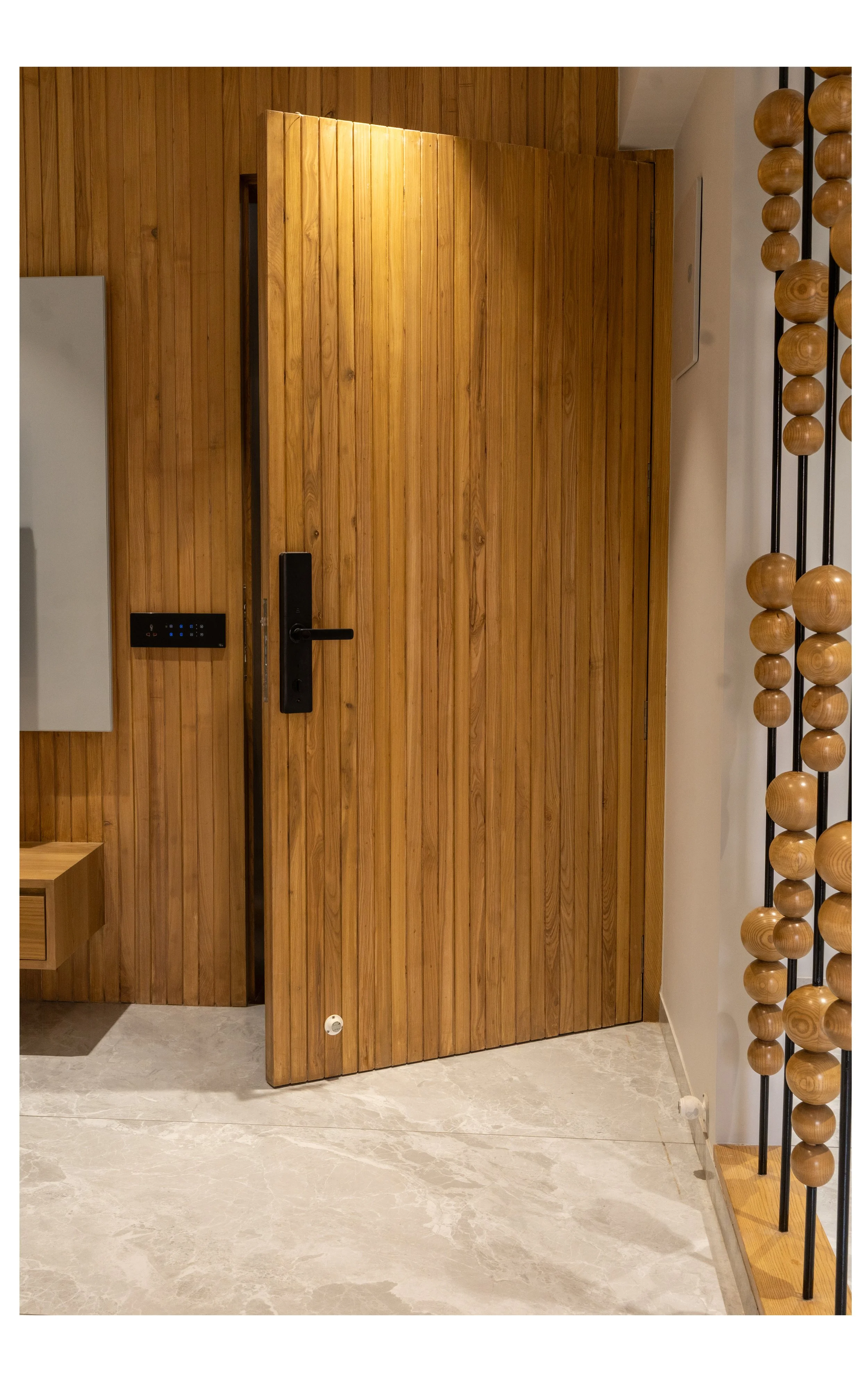 Interior space with a wooden door, black handle, keypad, a white wall on the right, and a decorative wooden bead structure on the right side.