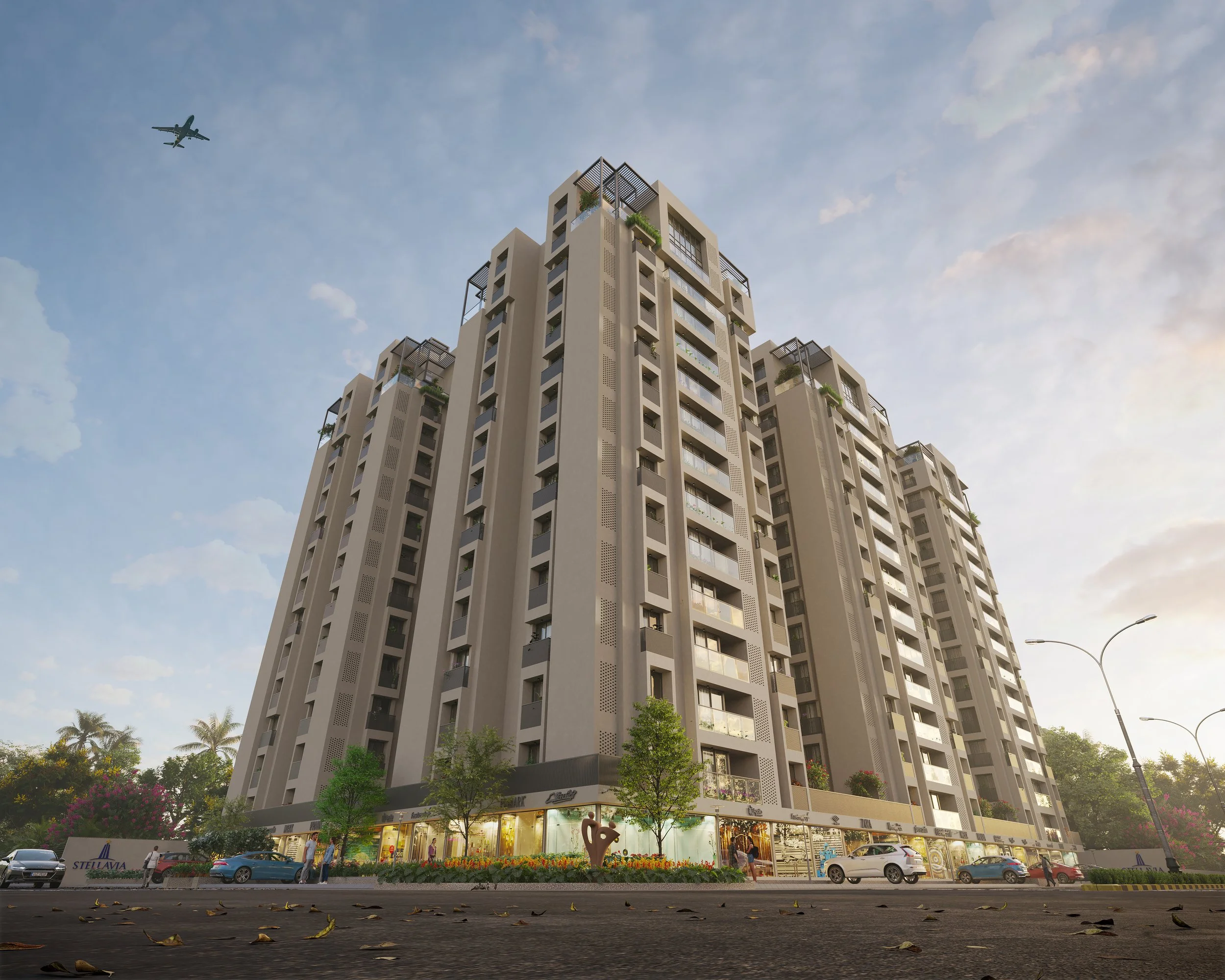 A large modern multi-story residential building with commercial shops on the ground floor, surrounded by cars and trees, with an airplane flying overhead in a partly cloudy sky.