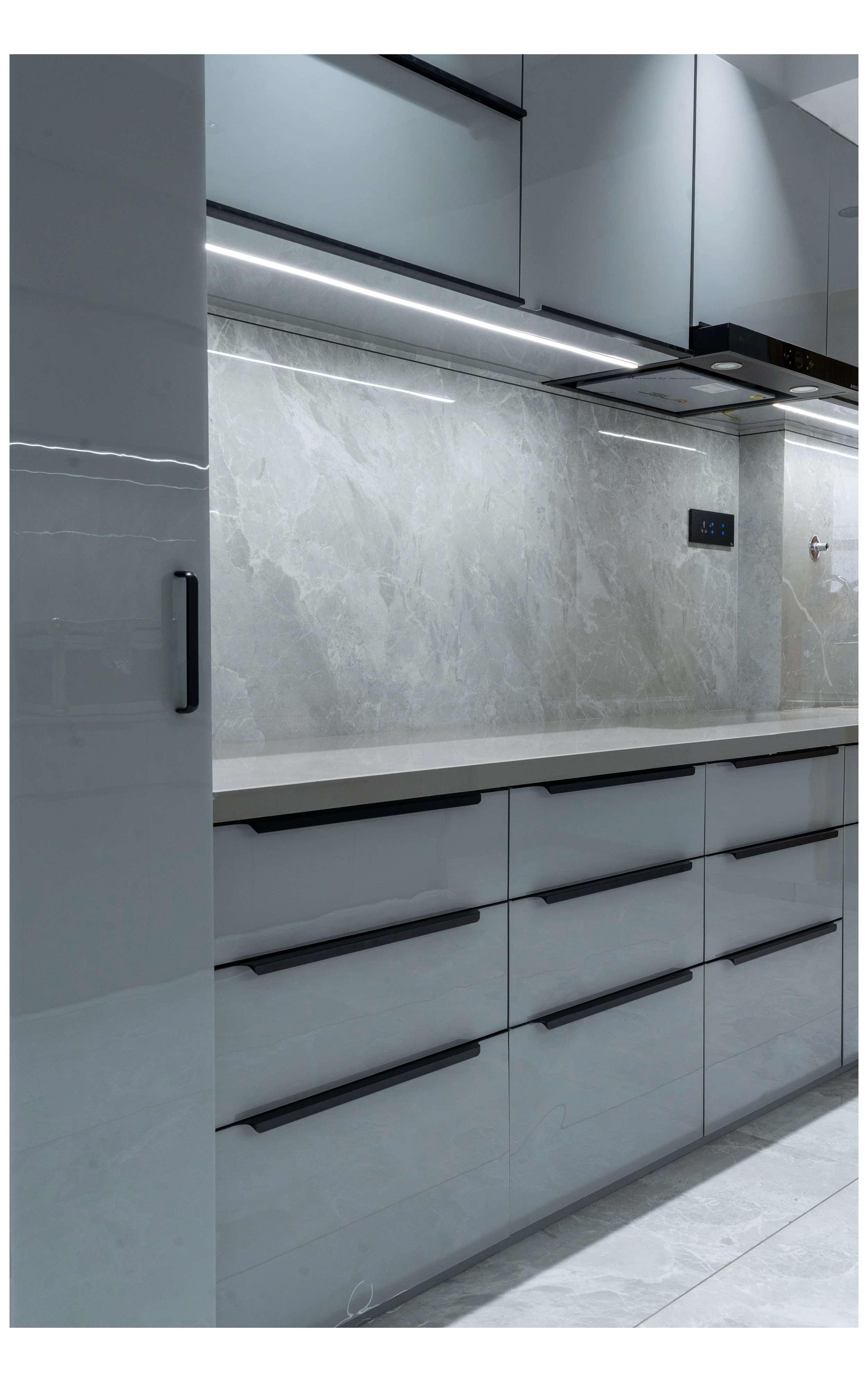 Modern kitchen with glossy grey cabinets, grey marble countertops, and grey marble backsplash, featuring black cabinet handles and under-cabinet lighting.