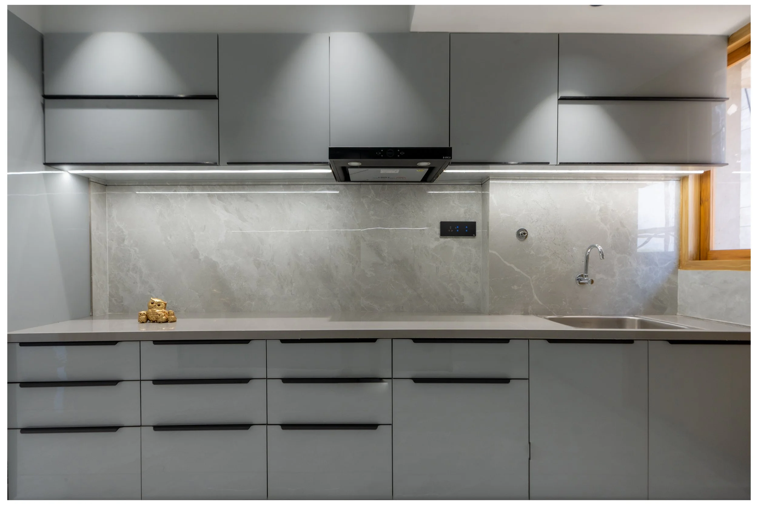 Modern kitchen with gray cabinets, marble backsplash, a small gold owl figurine on the countertop, and a window on the right side.