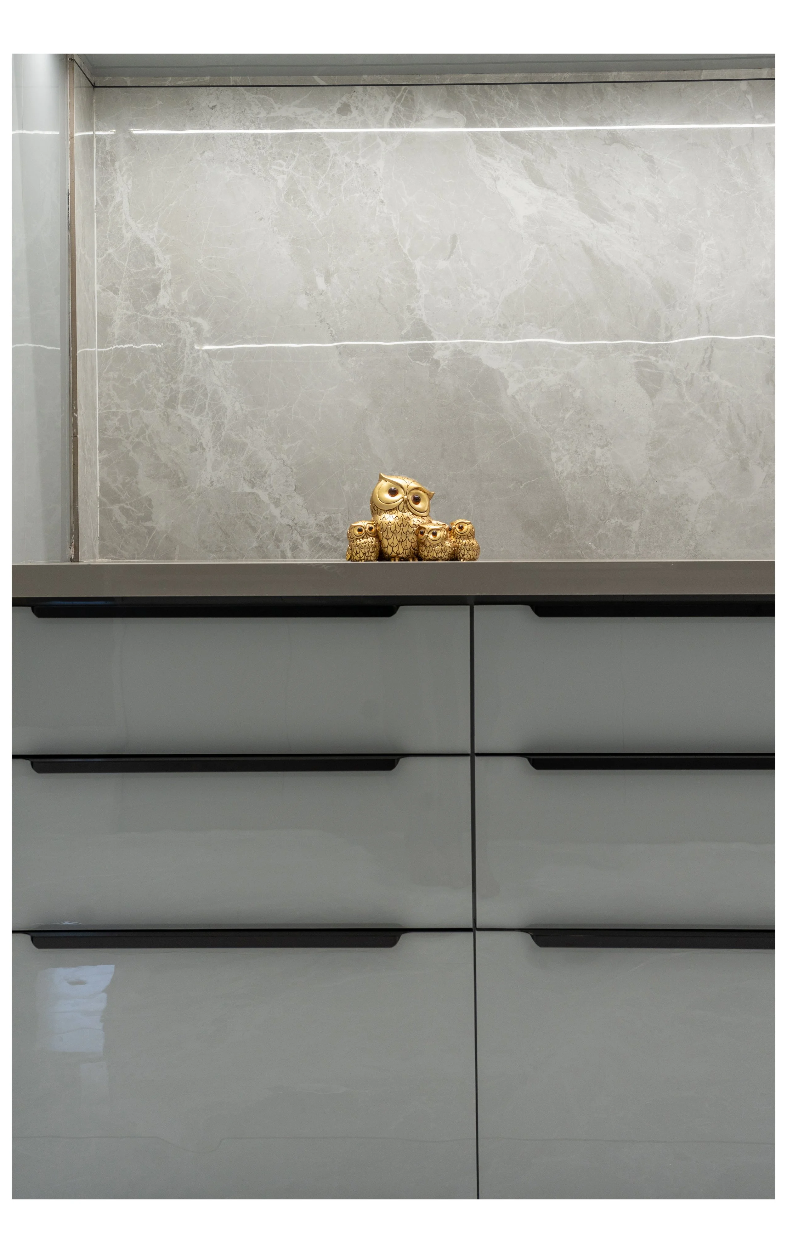 Gold owl figurine with three smaller owl figurines placed on a gray countertop in front of a marble wall.