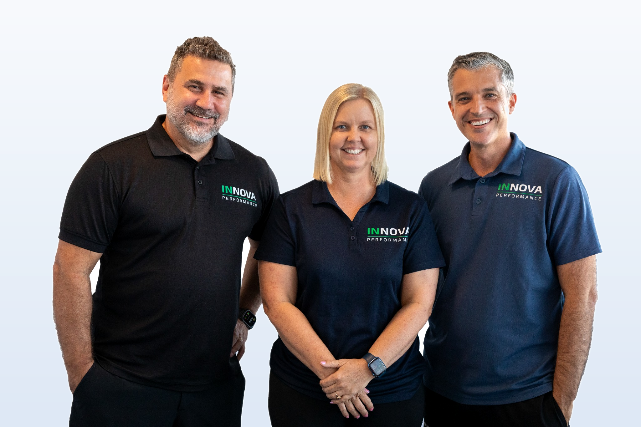 Three smiling team members wearing navy and black polo shirts with the INNOVA Performance logo, standing against a light background.