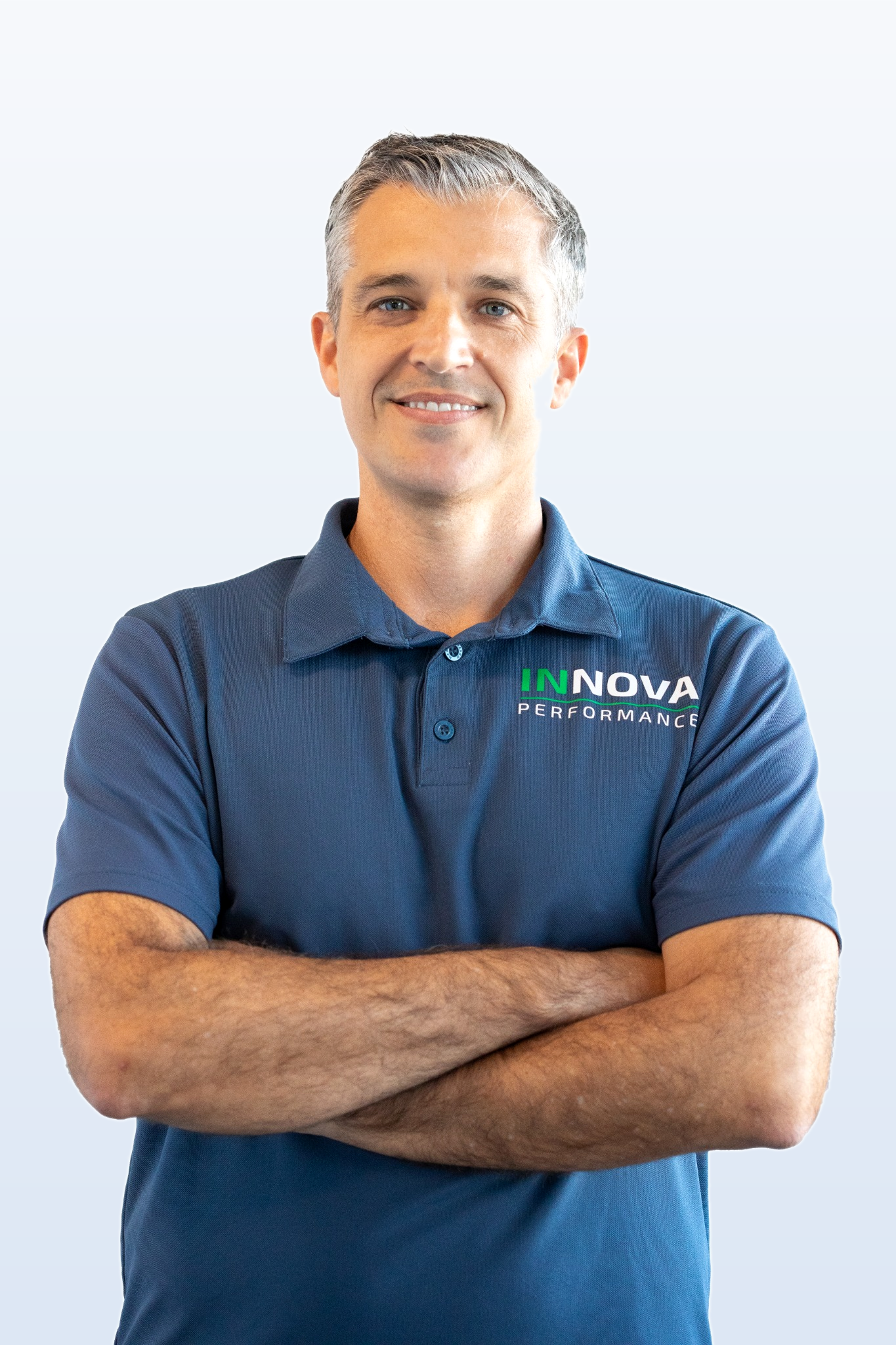 A man with short gray hair, wearing a blue polo shirt with the logo 'INNOVA PERFORMANCE' on it, standing with crossed arms and smiling against a plain light background.
