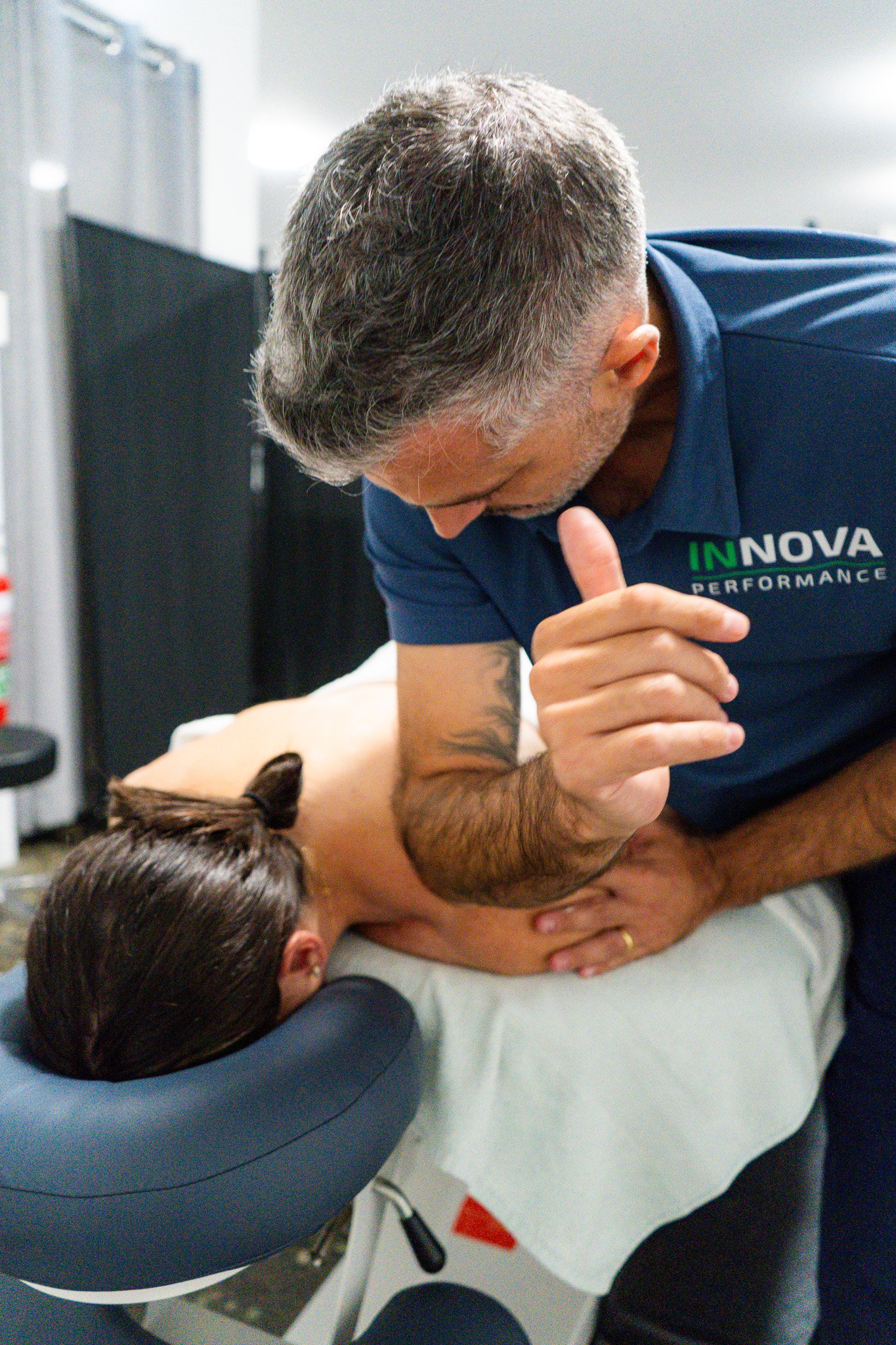 A chiropractor performing a spinal adjustment on a patient lying face down on a chiropractic table in a clinical setting.