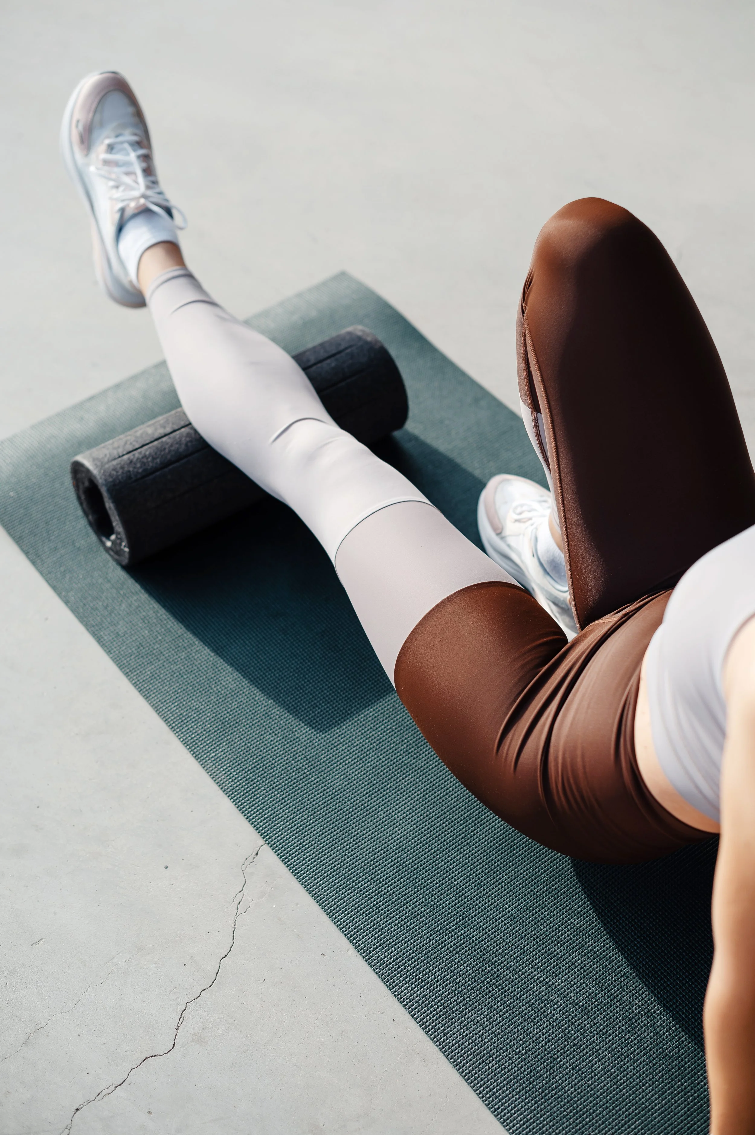 Person stretching their leg on a foam roller while lying on a yoga mat in a gym.