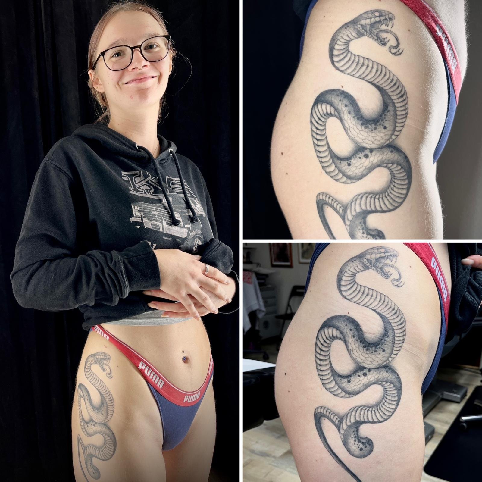 Junge Frau mit Brille und Hoodie, zeigt den Bauch mit Tattoo eines Schlangenmotivs auf der Seite.