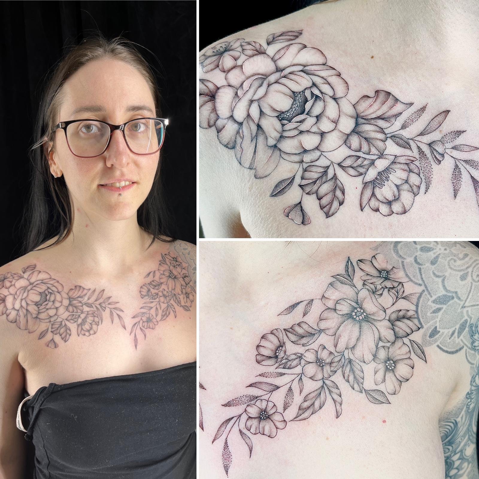 Eine Frau mit Brille und Piercing zeigt eine Tätowierung von Blumen auf der Schulter und im Dekolleté, bestehend aus großflächigen, detailreichen Blüten und Blättern.