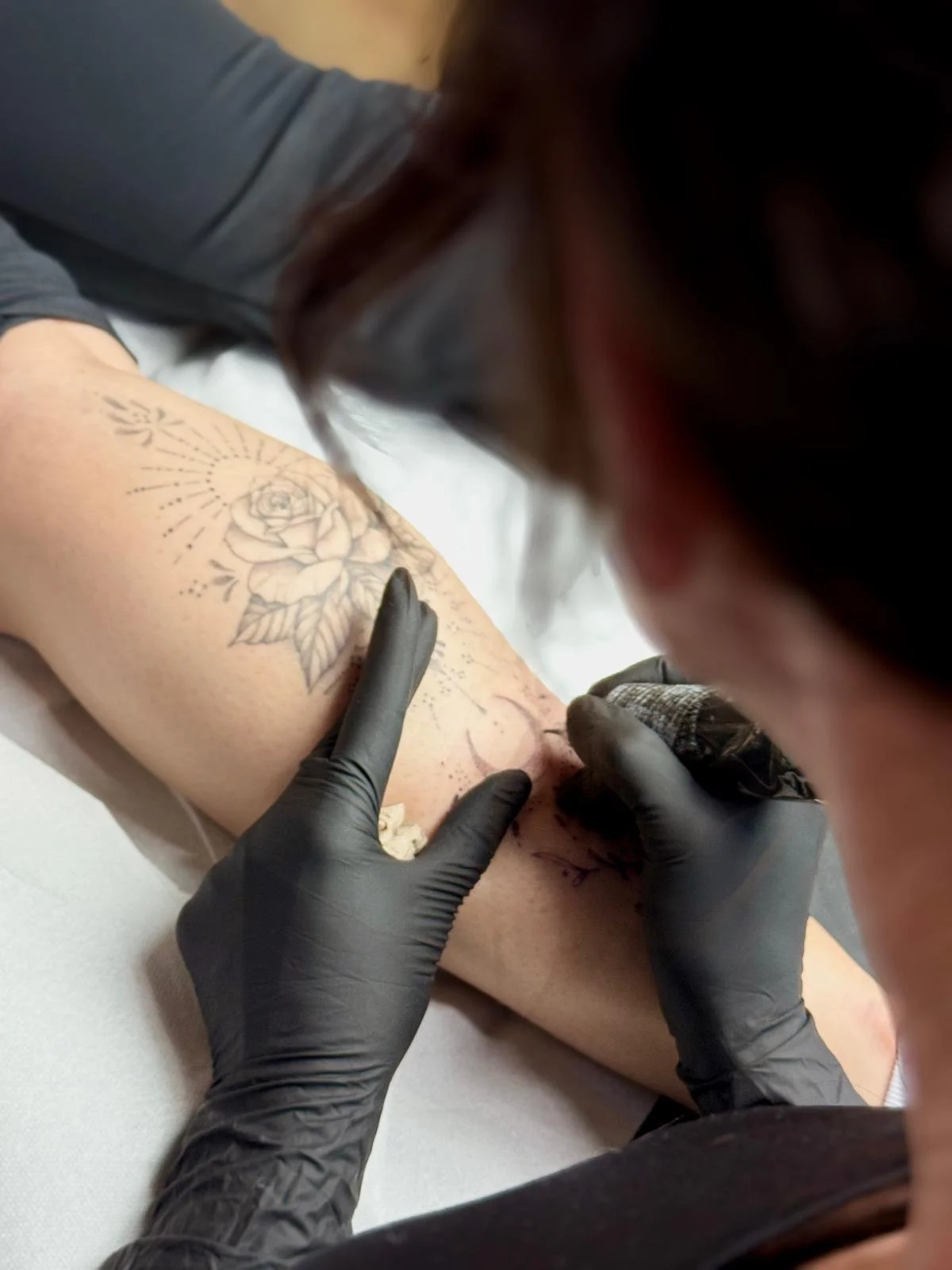 Tattoo-Künstler, der eine Rose auf den Oberschenkel eines Kunden tätowiert.