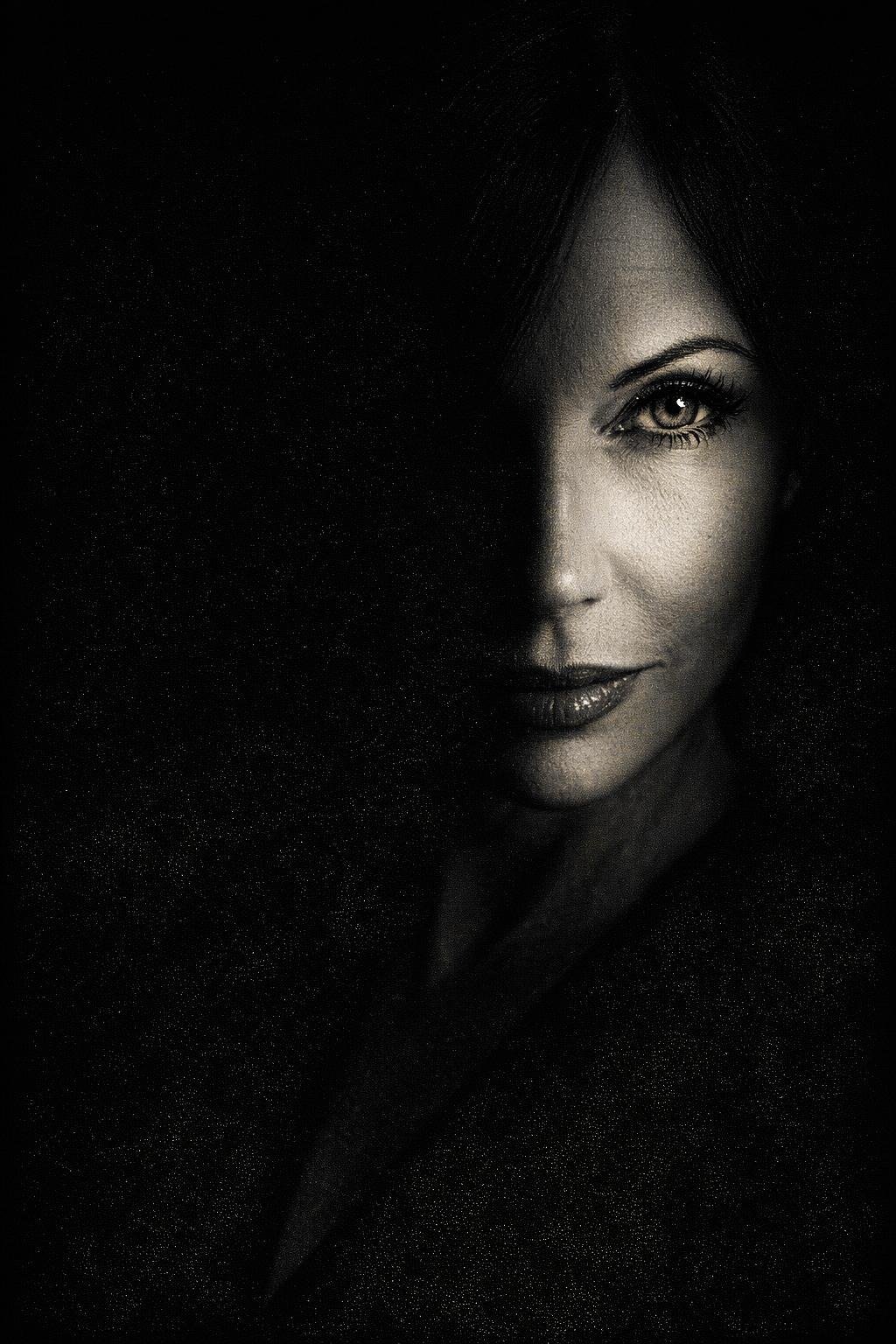 Schwarz-weiß Porträt einer Frau, halb im Schatten, mit betonter Gesichtshälfte, helle Augen, makeup, dunkle Lippen, elegant.