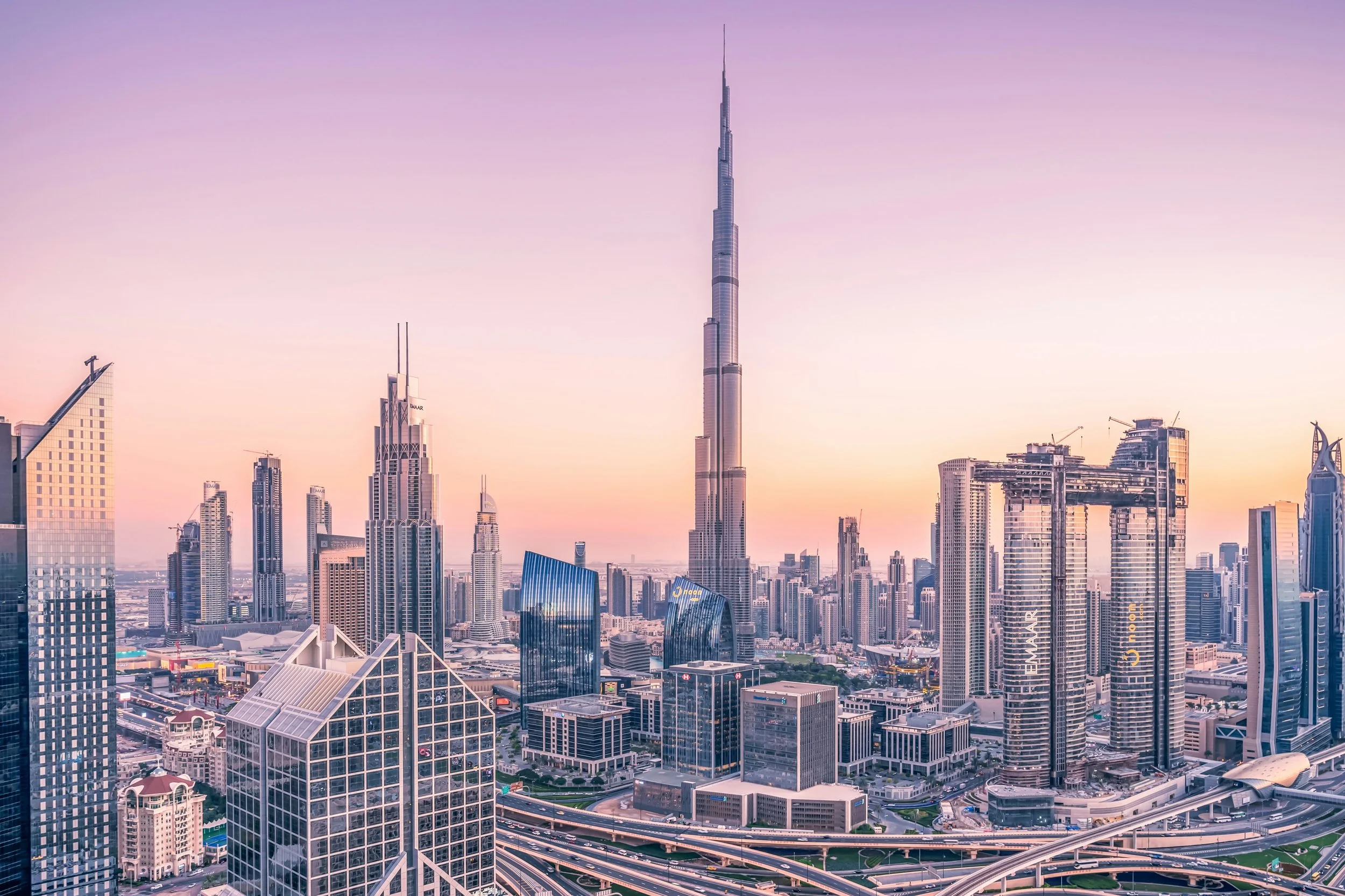 Skyline of Dubai with the Burj Khalifa towering among modern skyscrapers at sunset.