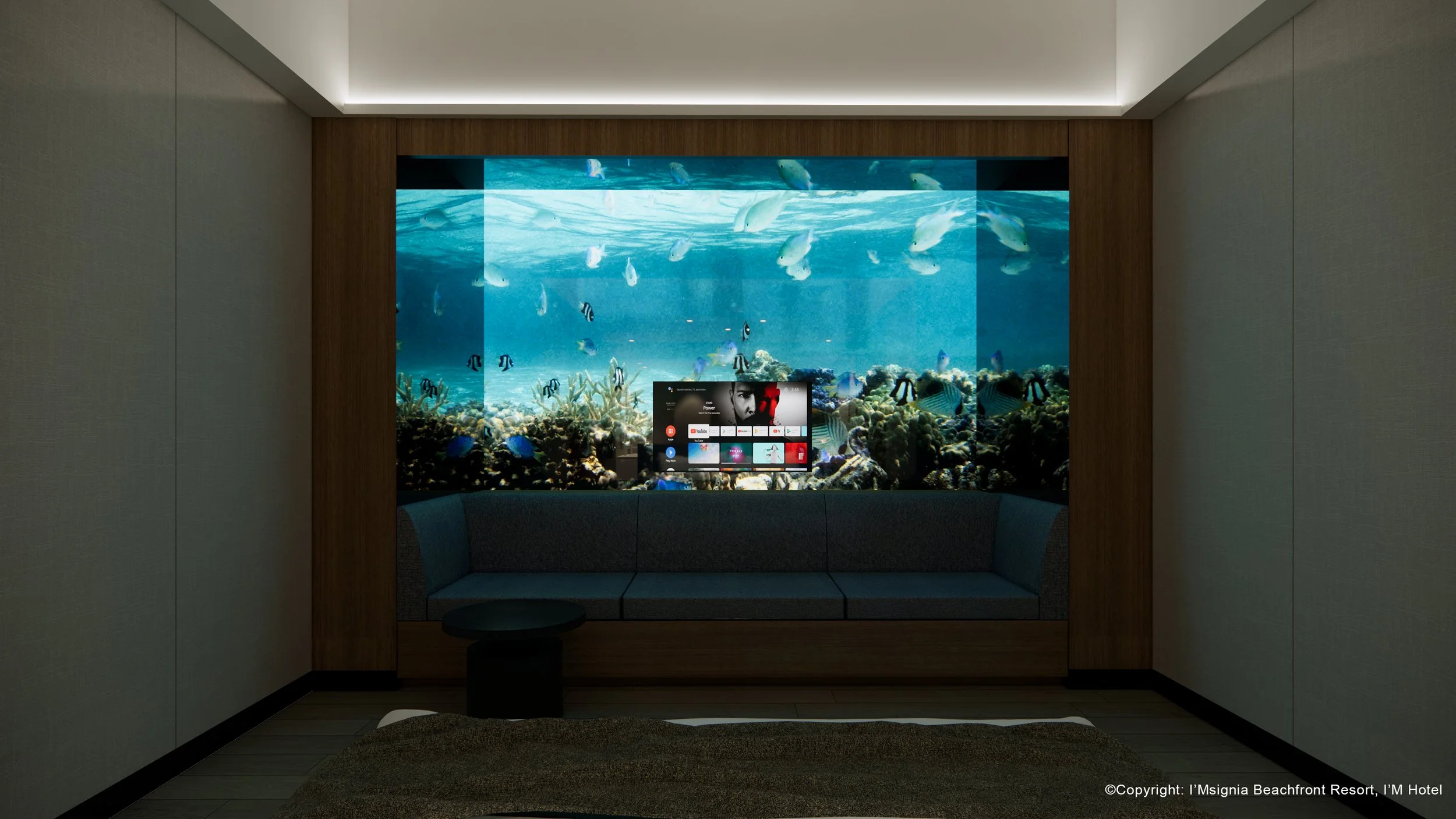 A hotel room with a large aquarium built into the wall behind a sofa, featuring various tropical fish and coral.