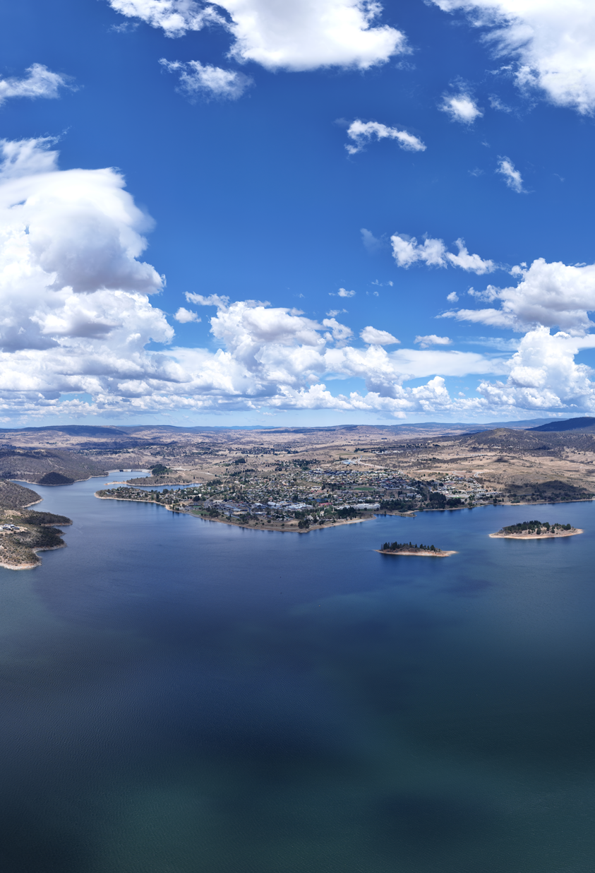 Aerial view of a lake with several small islands and a town along the shoreline under a partly cloudy blue sky.