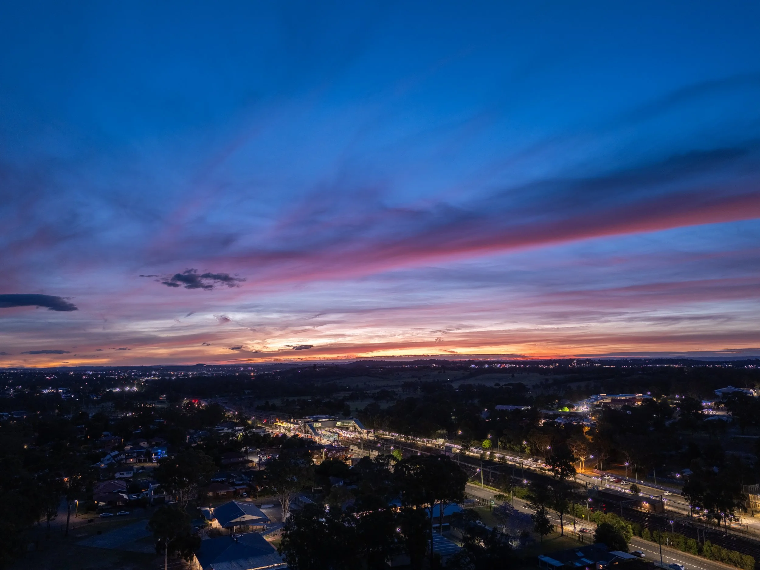Sunset over a city with colorful sky, illuminated streets, and buildings.