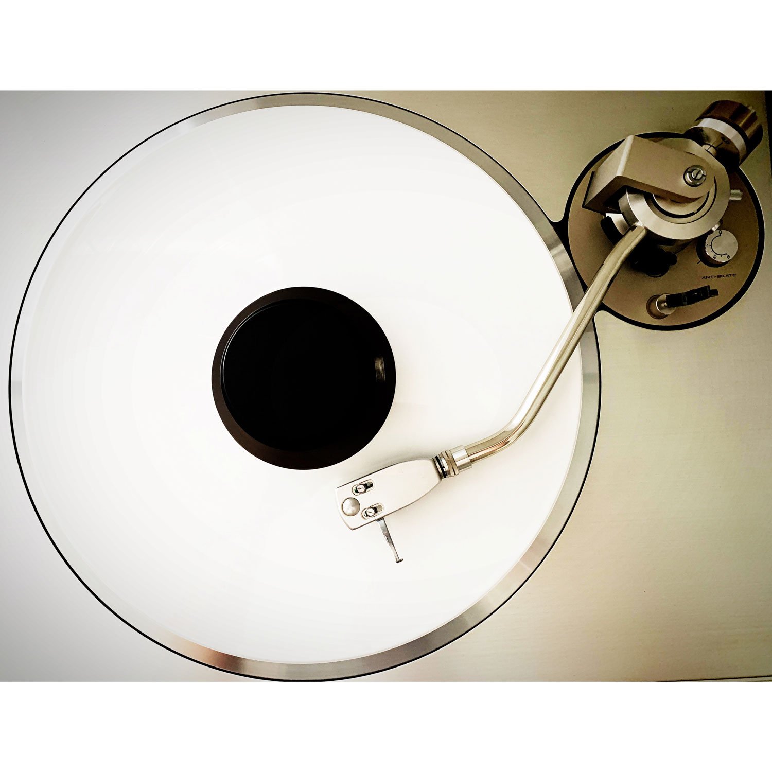 Close-up of a turntable with a white platter, black center circle, and a silver tonearm.