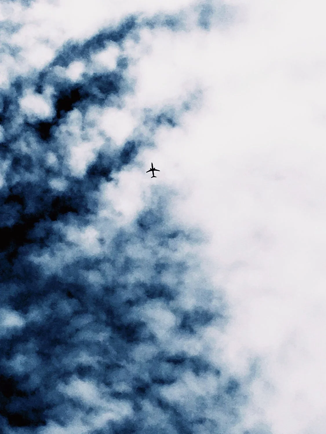 An airplane flying high in the sky among dark and white clouds.